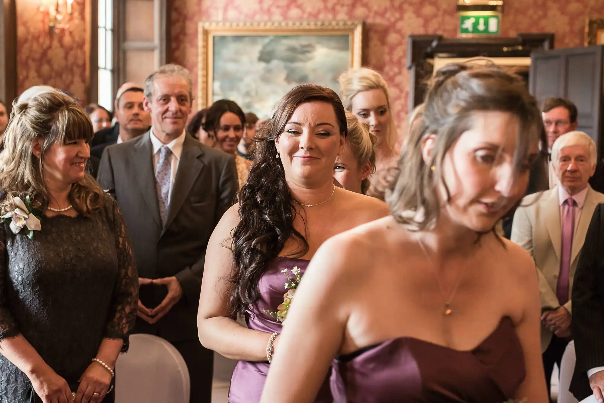 A wedding scene with guests looking on, focusing on a woman in a purple dress smiling emotionally.