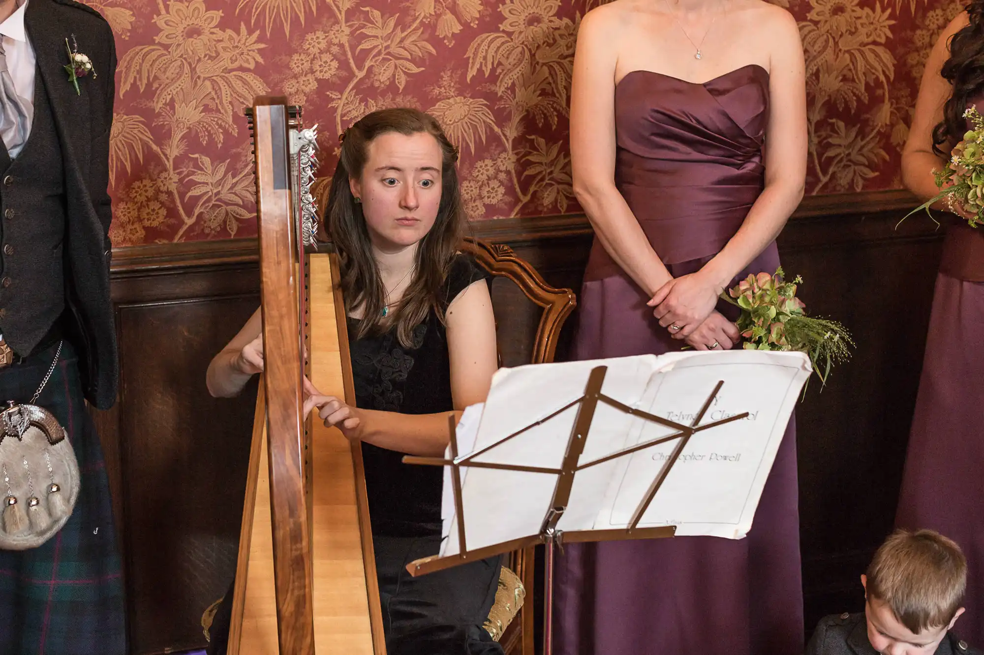 Woman in black dress playing a harp at an elegant event, with guests in formal attire observing the performance.
