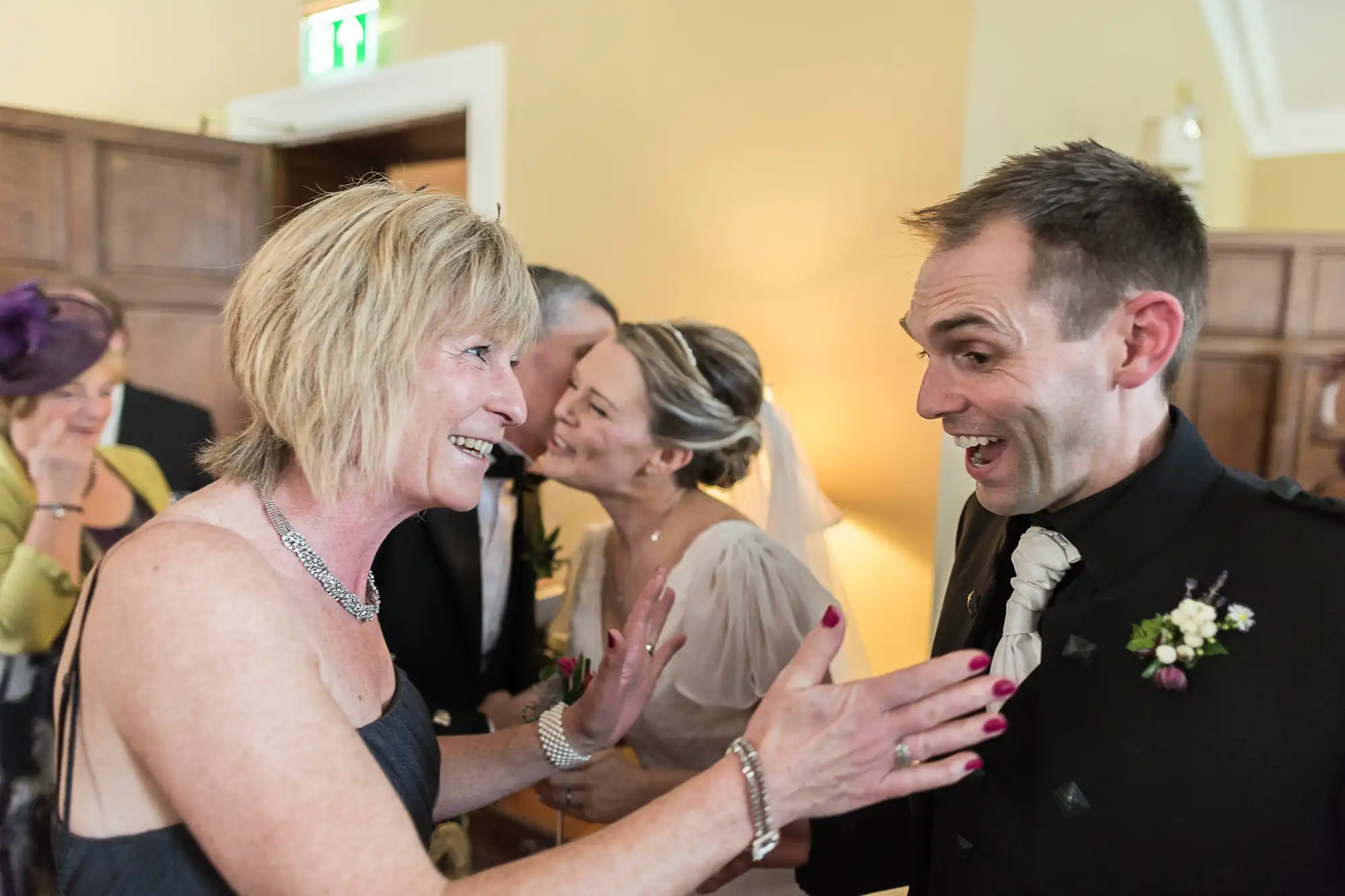 A joyful moment at a wedding reception, featuring a man in a black suit conversing animatedly with a smiling woman in a sleeveless dress.