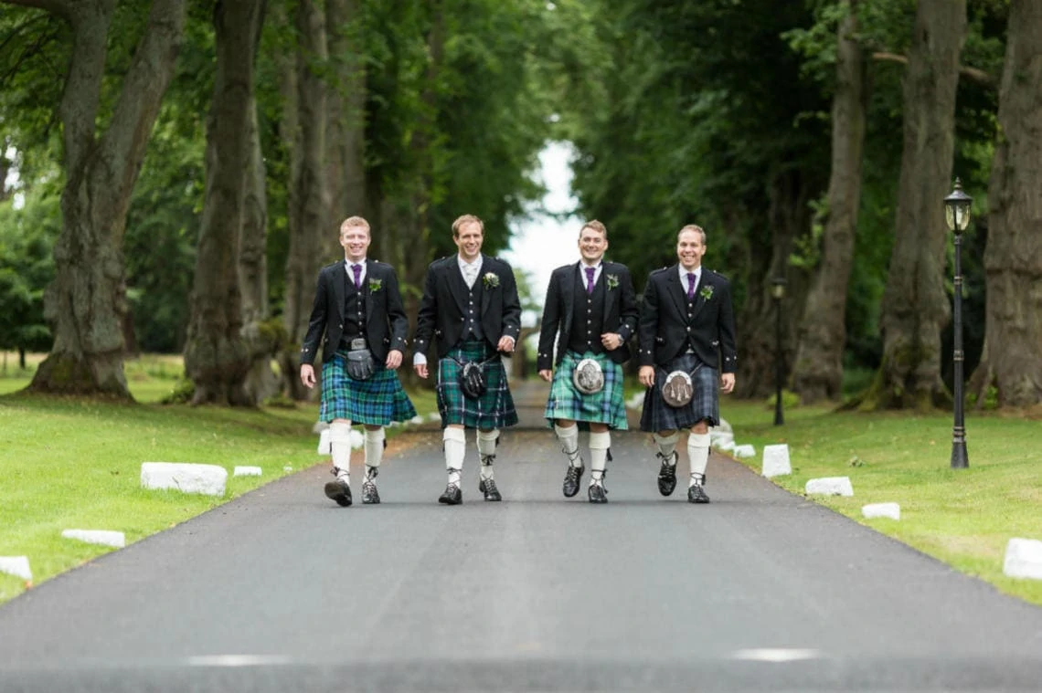 groom and groomsmen walking along the tree-lined approach