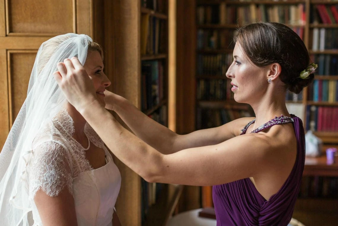 bridesmaid helps bride to put veil on in The Library