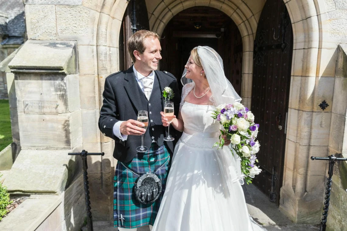 newlyweds with a glass of champagne at the entrance to Carberry Tower