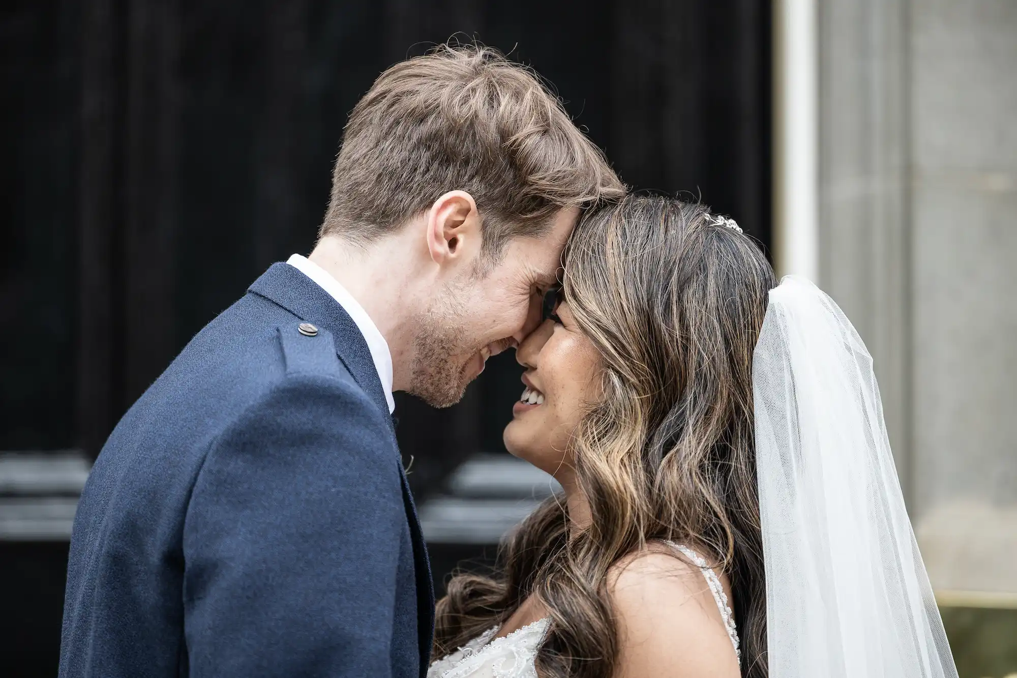 A bride and groom share a joyful moment at Carlowrie Castle , touching foreheads and smiling, on their wedding day.