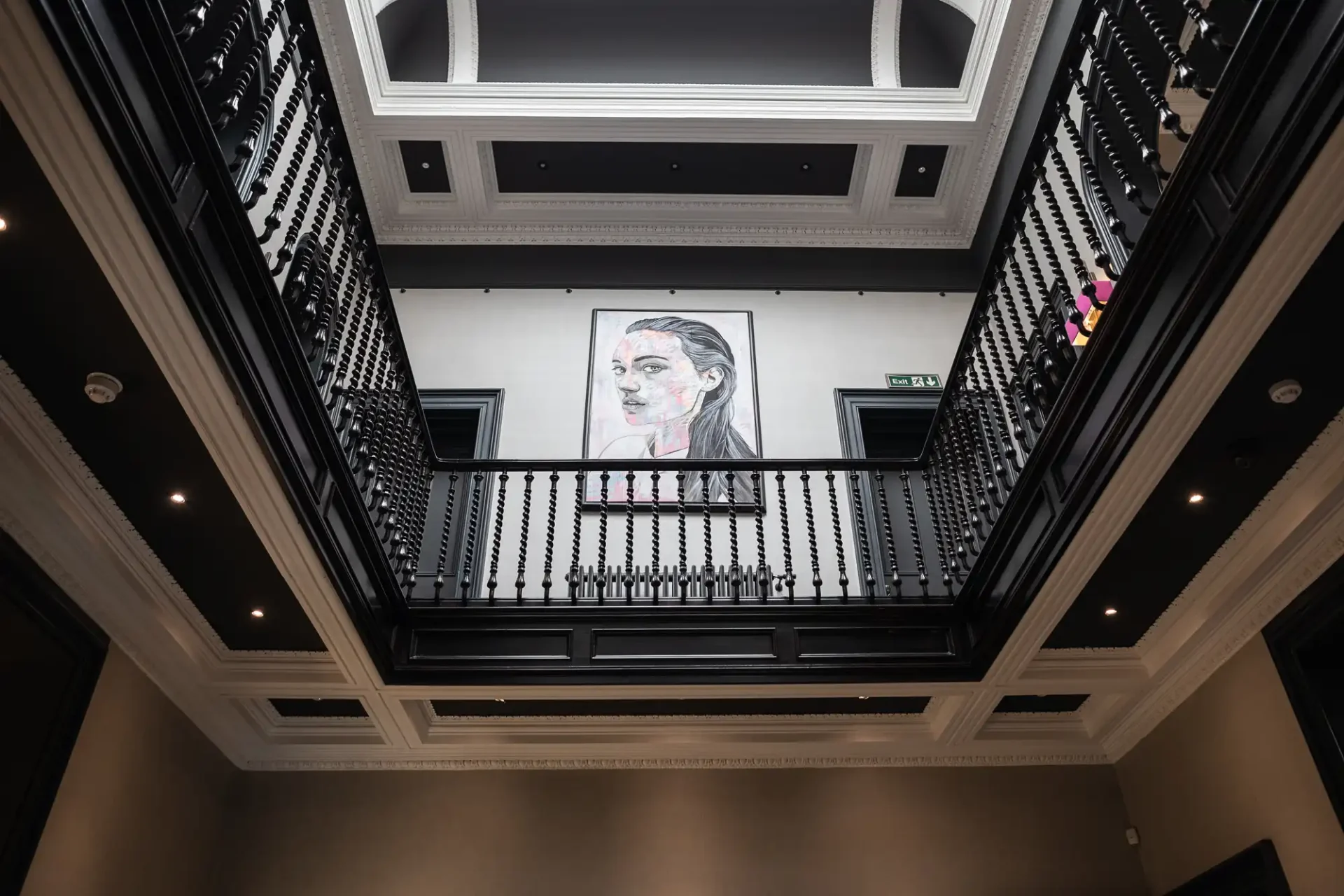 Interior of a multi-level atrium with black railings, white walls, and a large portrait hanging on the far wall above.