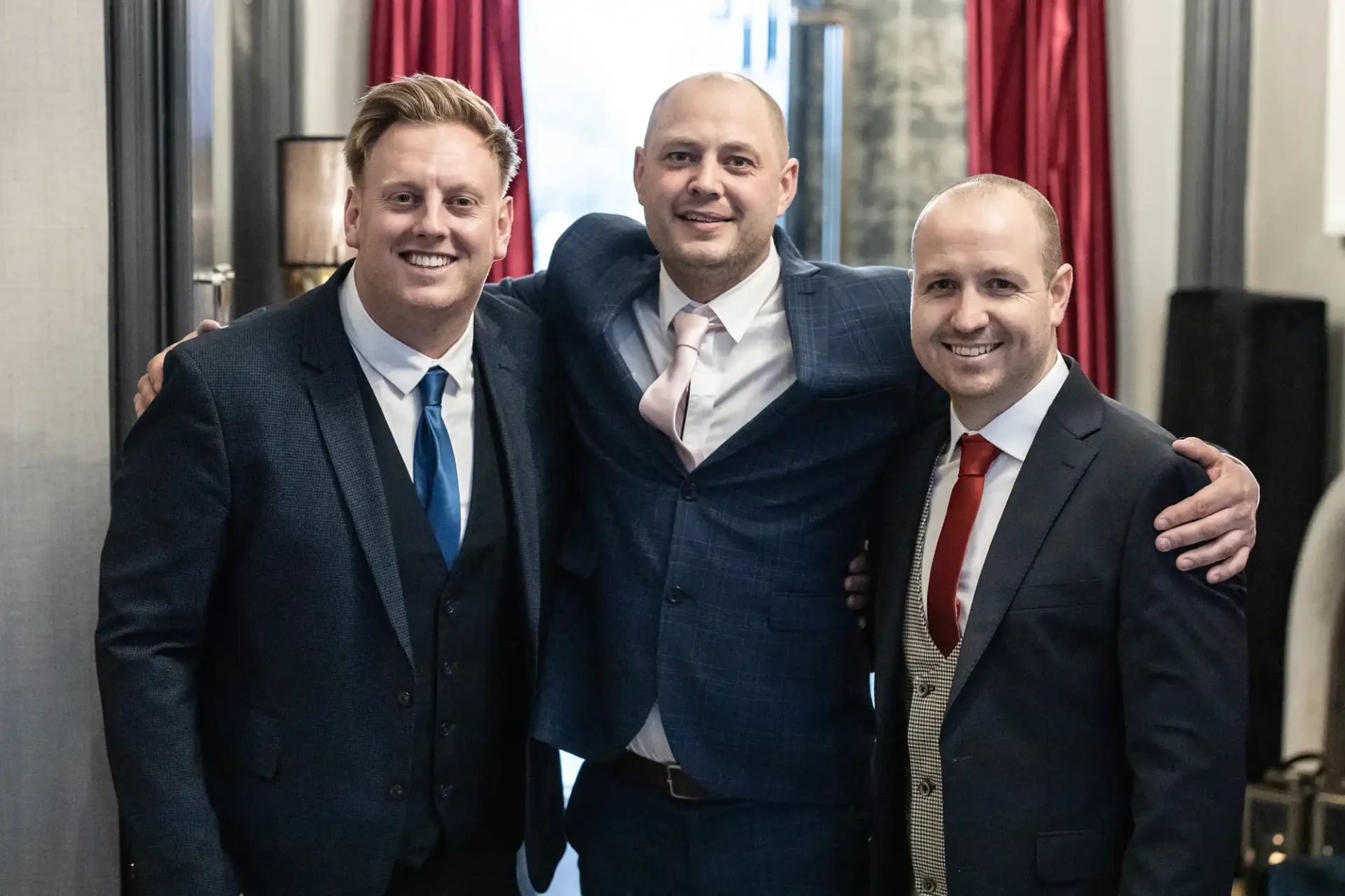 Three smiling men in business suits standing close together indoors.