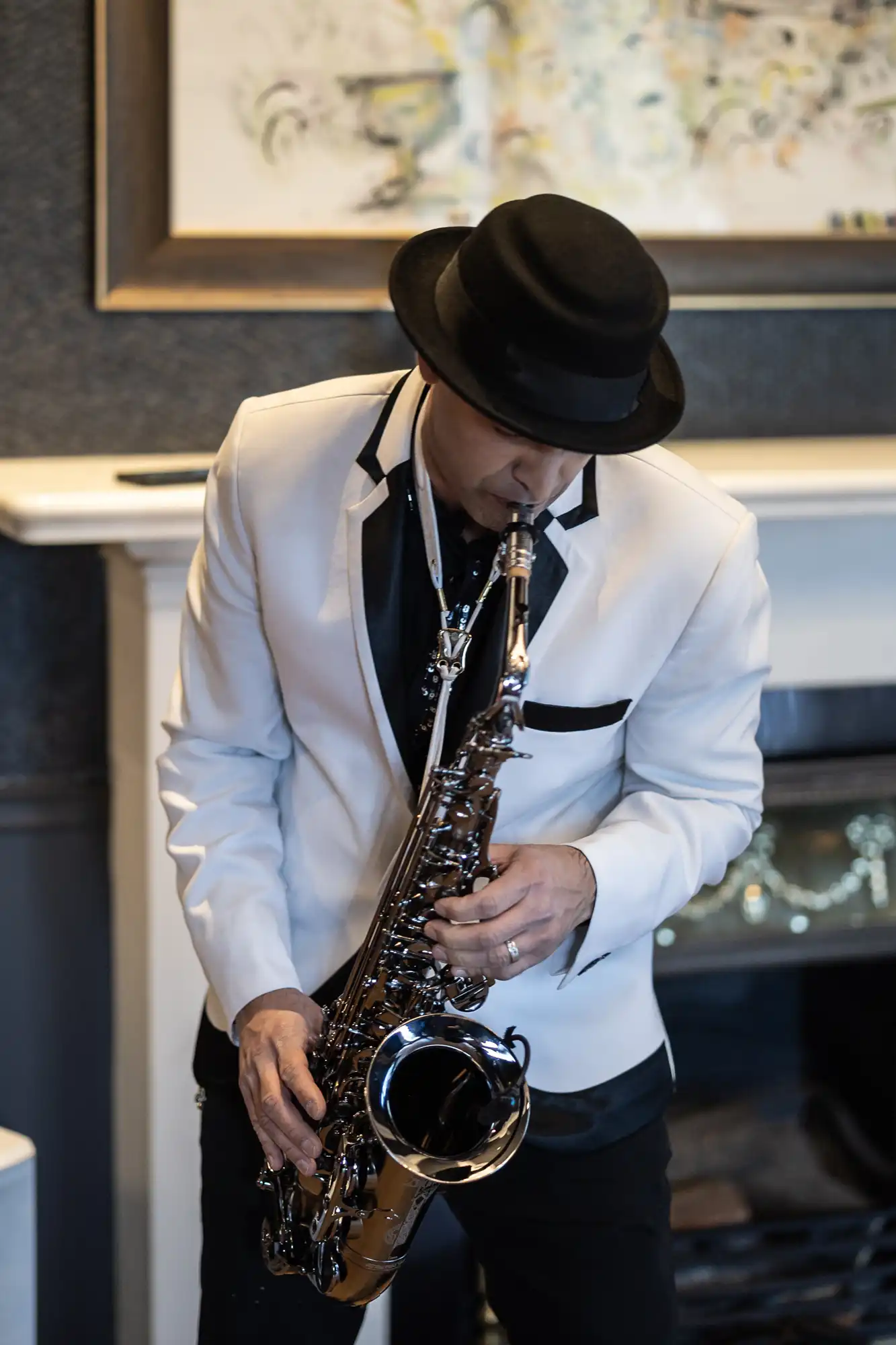 Man in a white jacket and black hat playing a saxophone indoors.