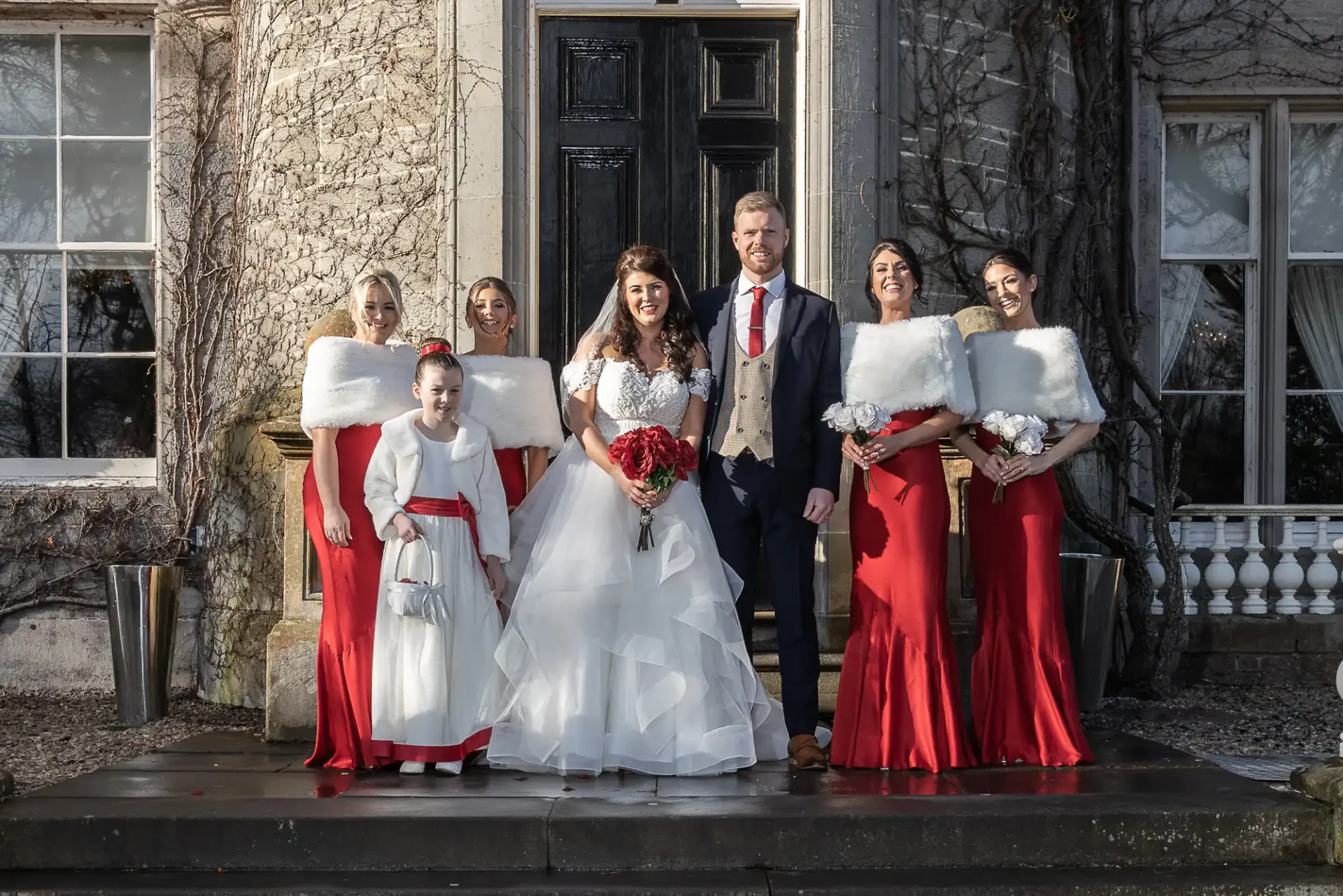 A bride and groom stand with five bridesmaids outside a historical building, all dressed in formal attire.