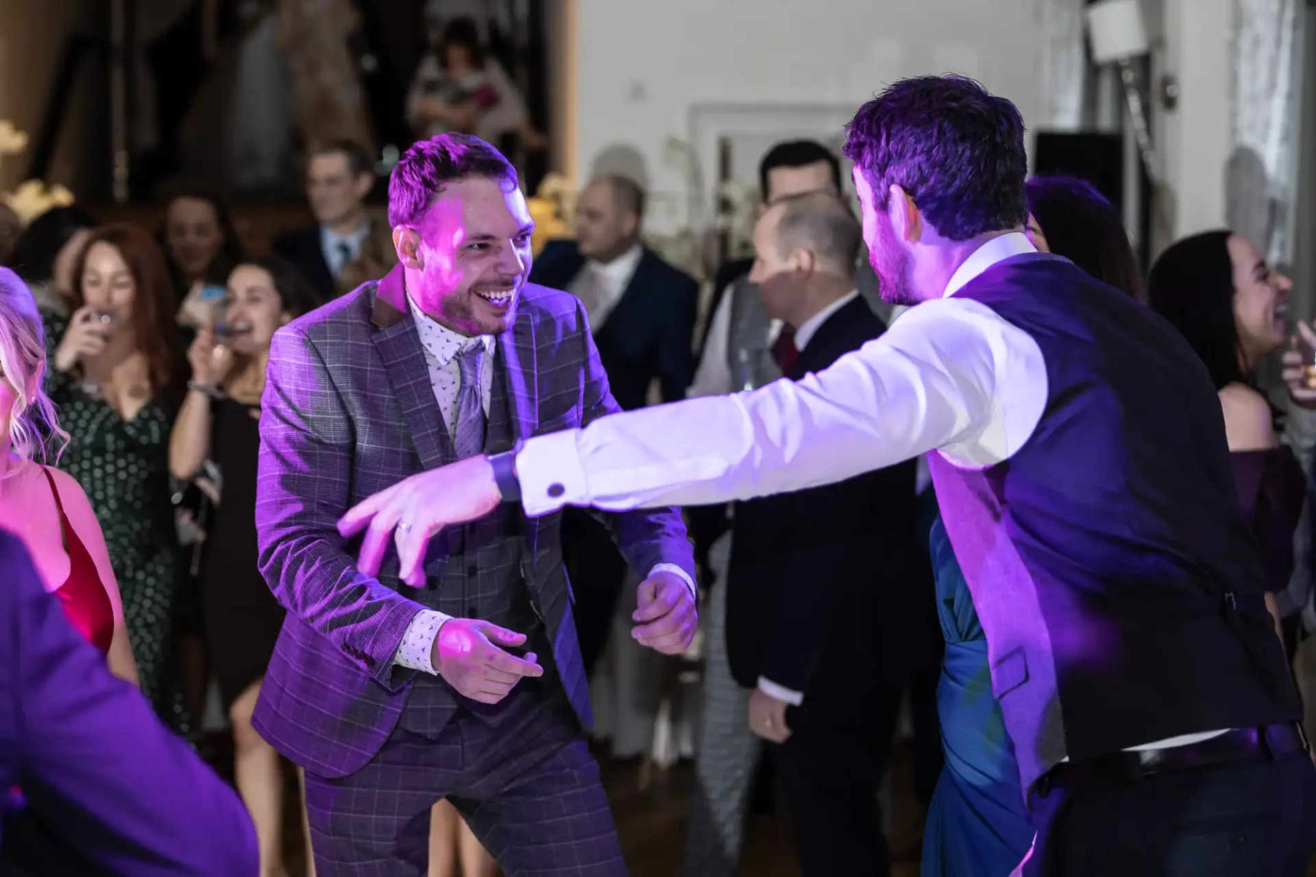 Two men dancing joyfully at a lively party with guests clapping around them.