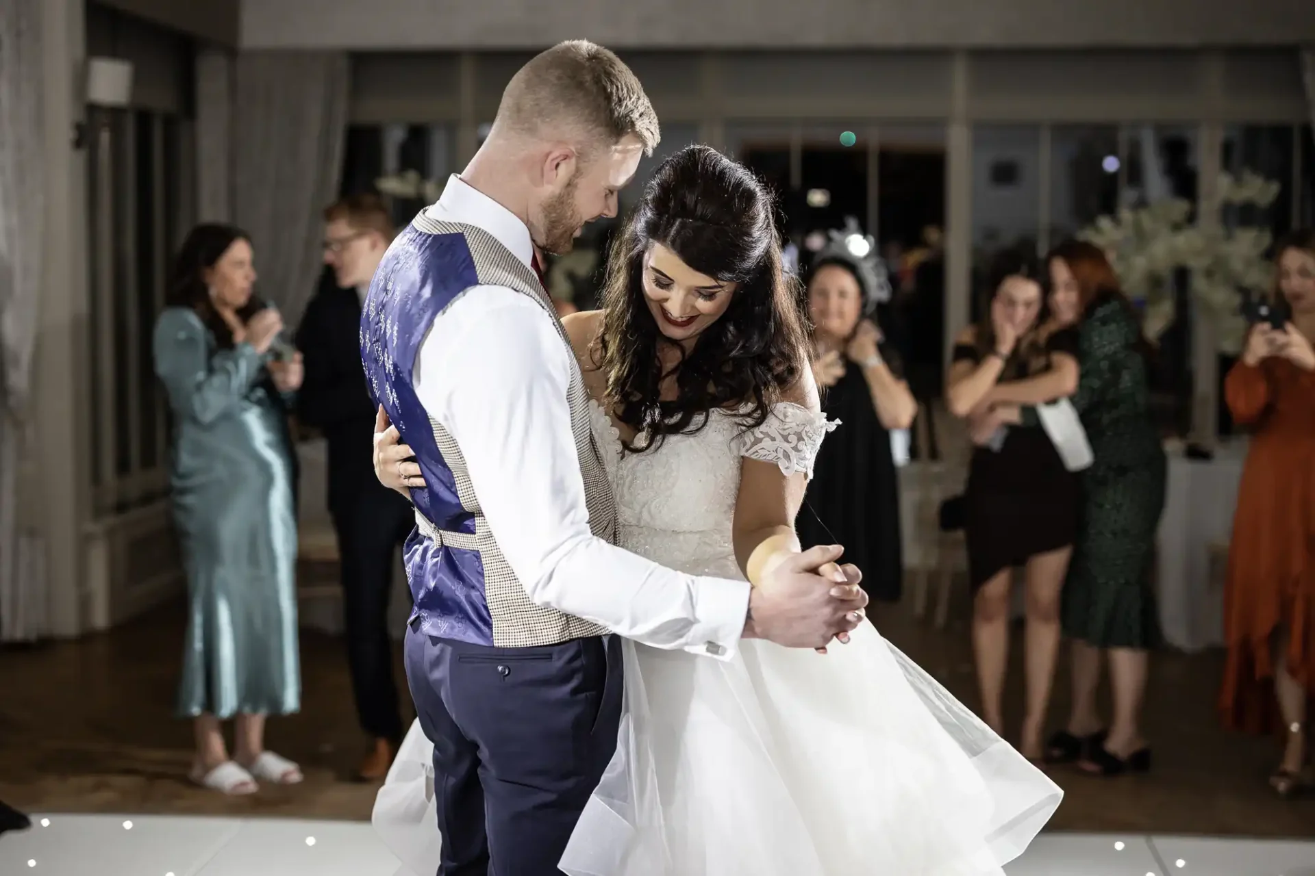 Bride and groom share their first dance at a wedding reception, surrounded by guests.