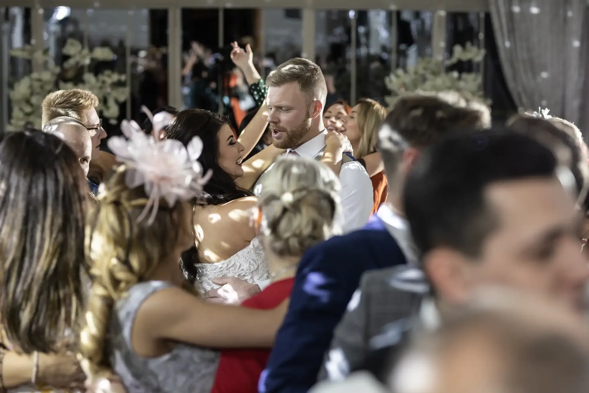 A joyful bride and groom kiss while dancing at their wedding reception, surrounded by cheerful guests.