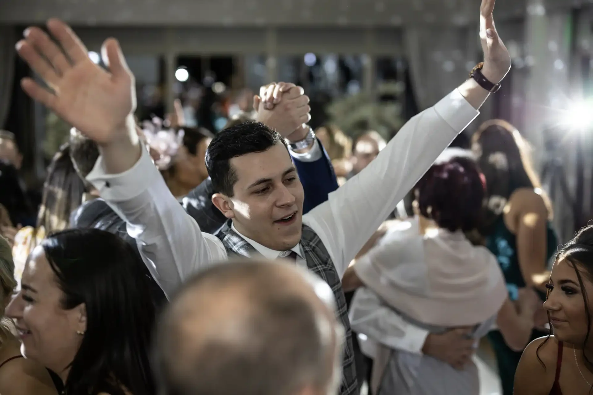 Man joyfully dancing with raised arms at a lively party surrounded by other guests.