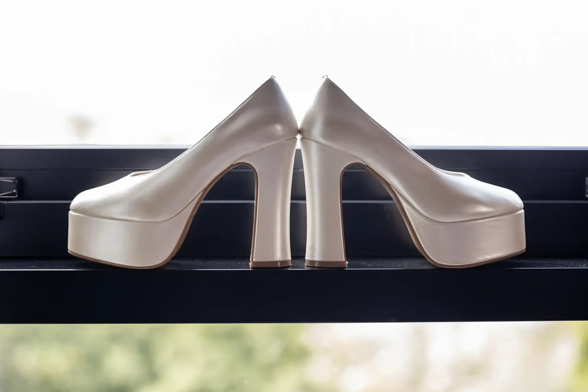 Pair of white platform high heel shoes placed back-to-back on a windowsill.