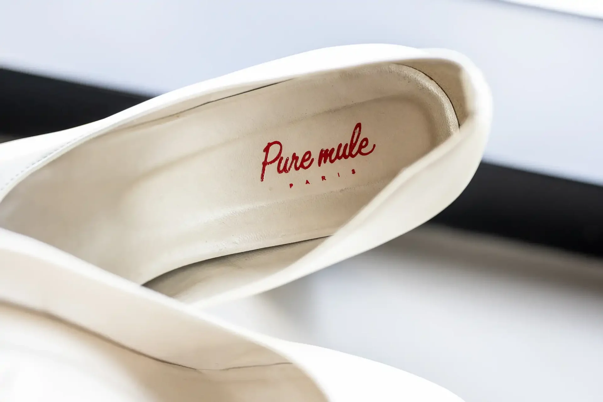 Close-up of white shoe insoles with red "Pure mule PARIS" text displayed.