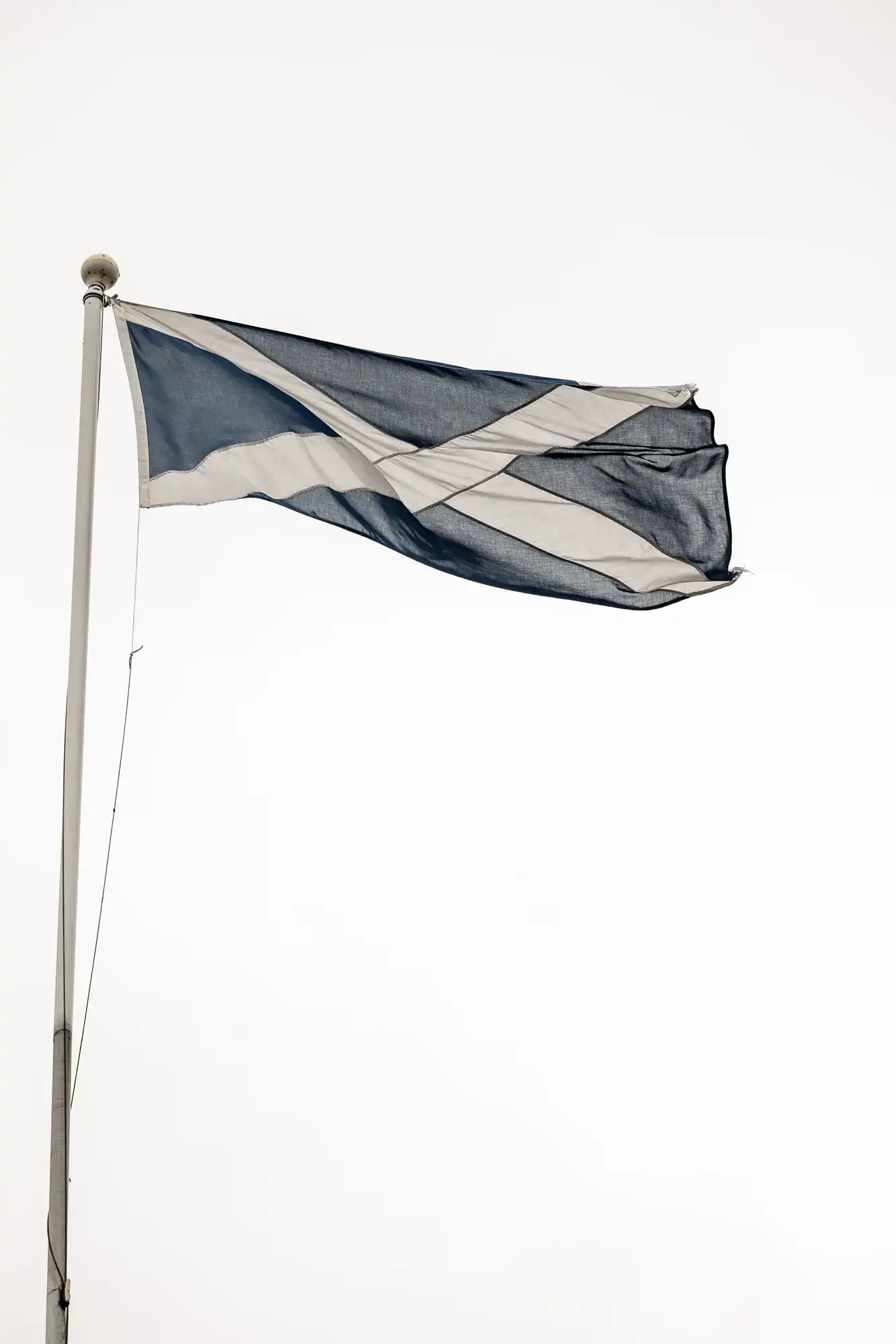 Scottish flag featuring a white saltire on a blue background, waving on a flagpole against a clear sky.