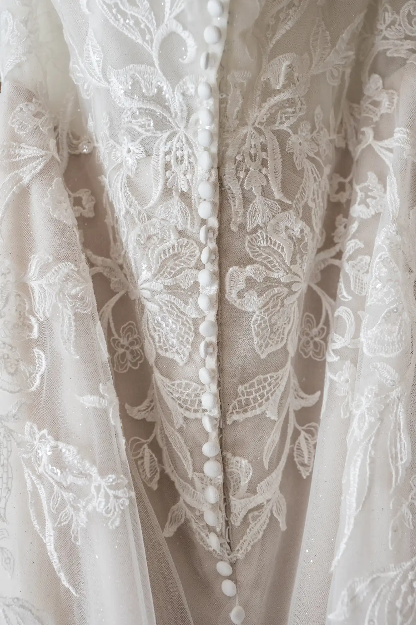 Close-up of a lace wedding dress bodice with floral patterns and a row of white buttons down the center.