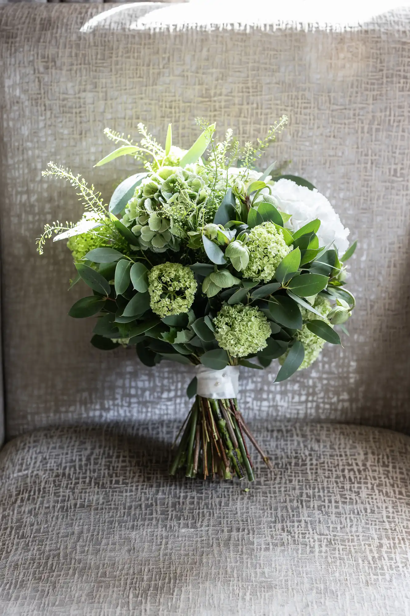 A bouquet of green and white flowers with leafy accents, tied with a white ribbon, rests on a textured gray background.