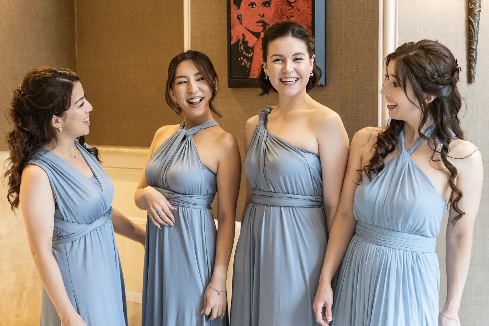 Four women in matching blue dresses stand indoors, smiling and conversing.