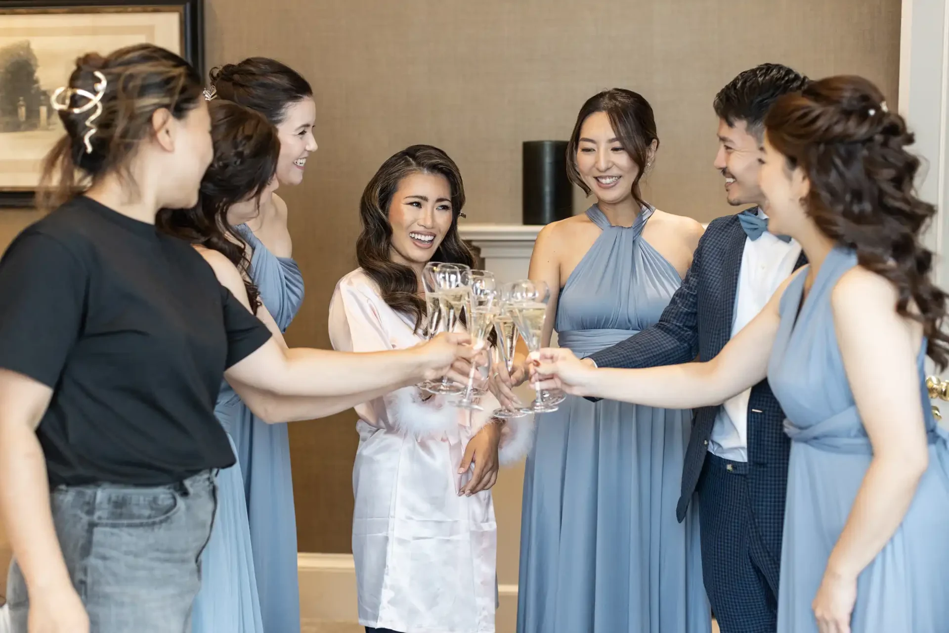 A group of people in formal attire toast with champagne flutes, smiling and standing indoors.