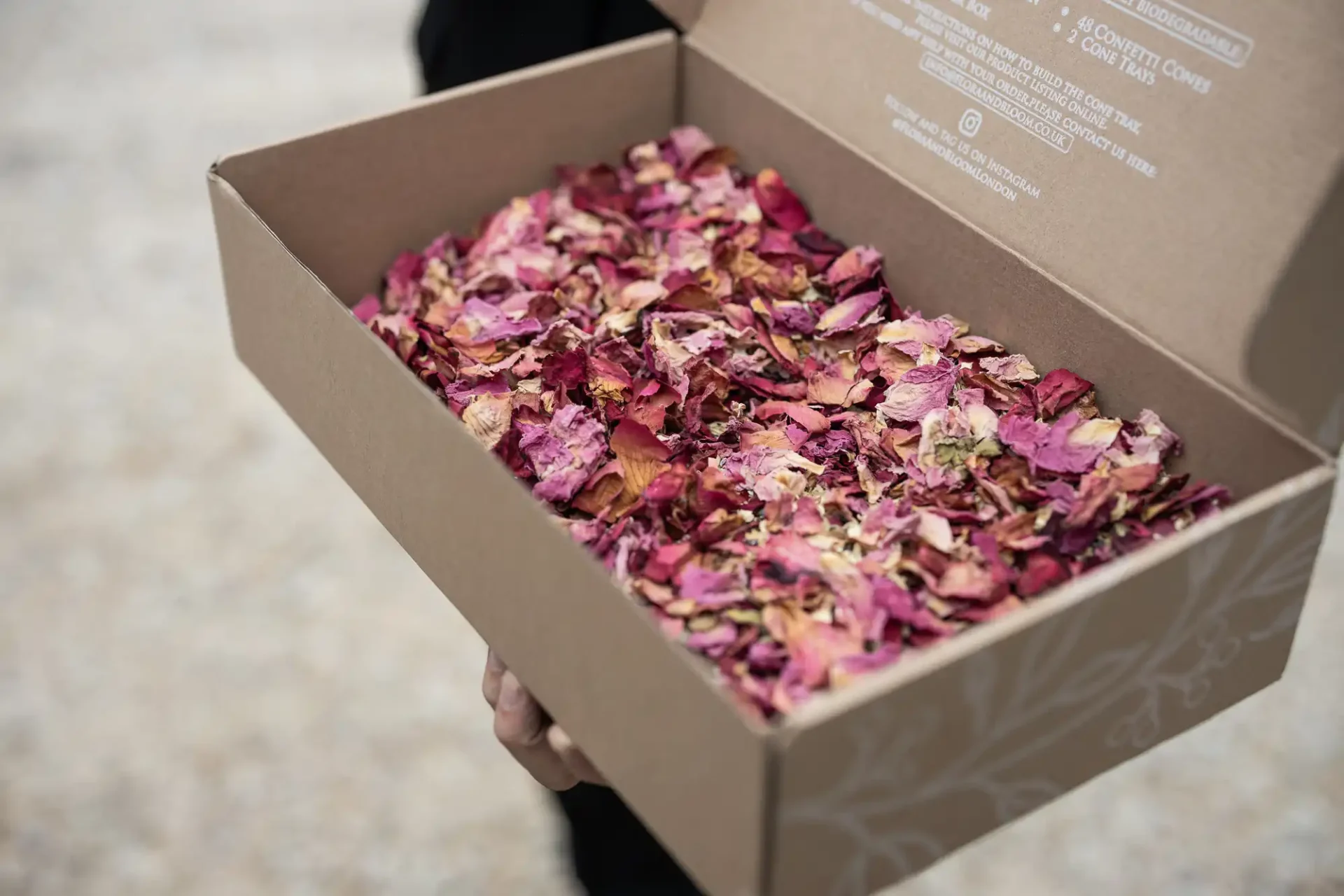 Box filled with dried rose petals, held by a person in a dark sleeve.