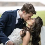 A bride and groom kiss outdoors. The groom is wearing a blue suit and the bride is in a white dress with a veil during their wedding at Carlowrie Castle.
