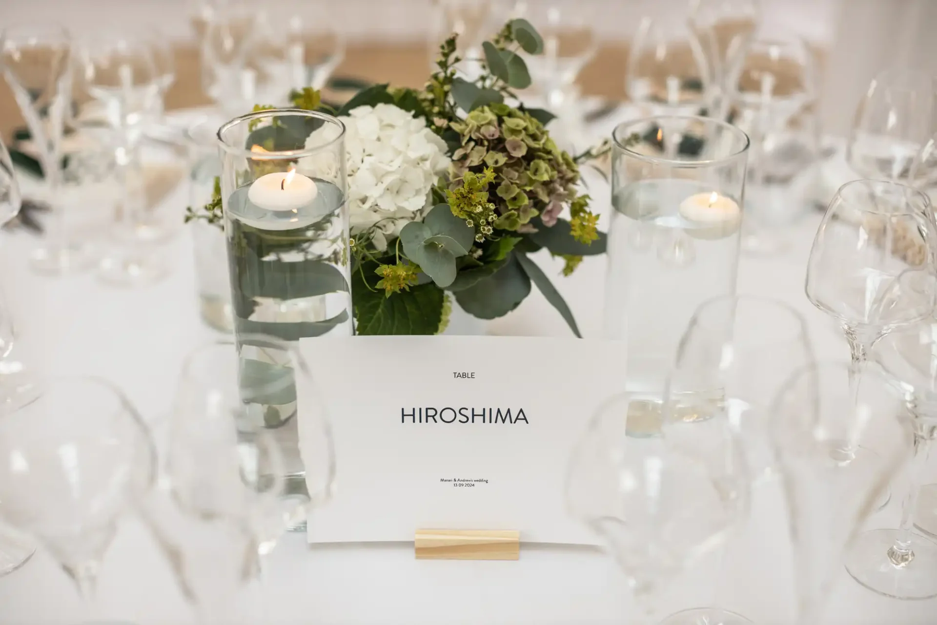 A table centerpiece with floating candles, white flowers, and green foliage surrounds a card labeled "Table Hiroshima.