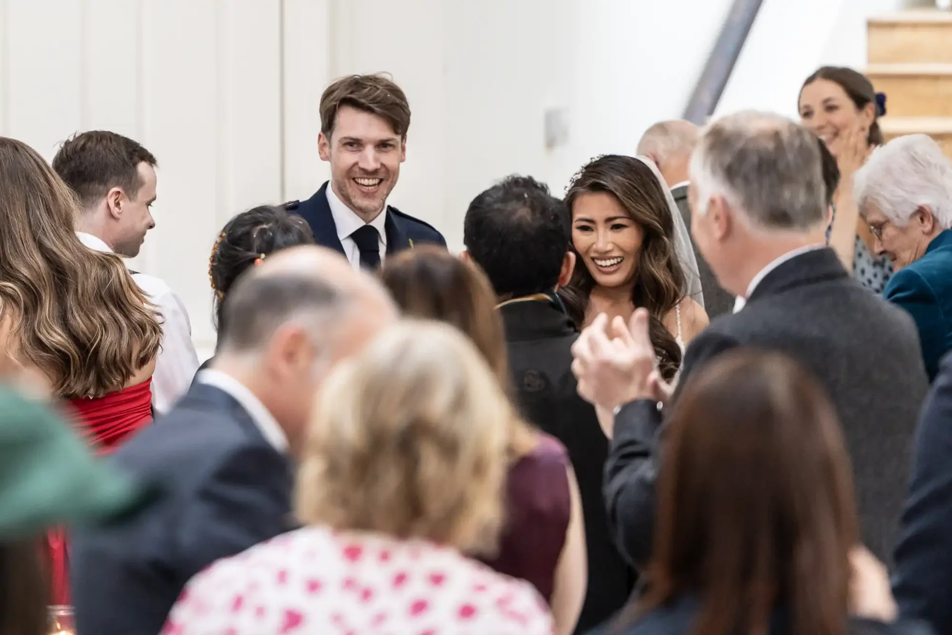 Guests mingling and chatting at a social event, focusing on a man and woman smiling and interacting with others.