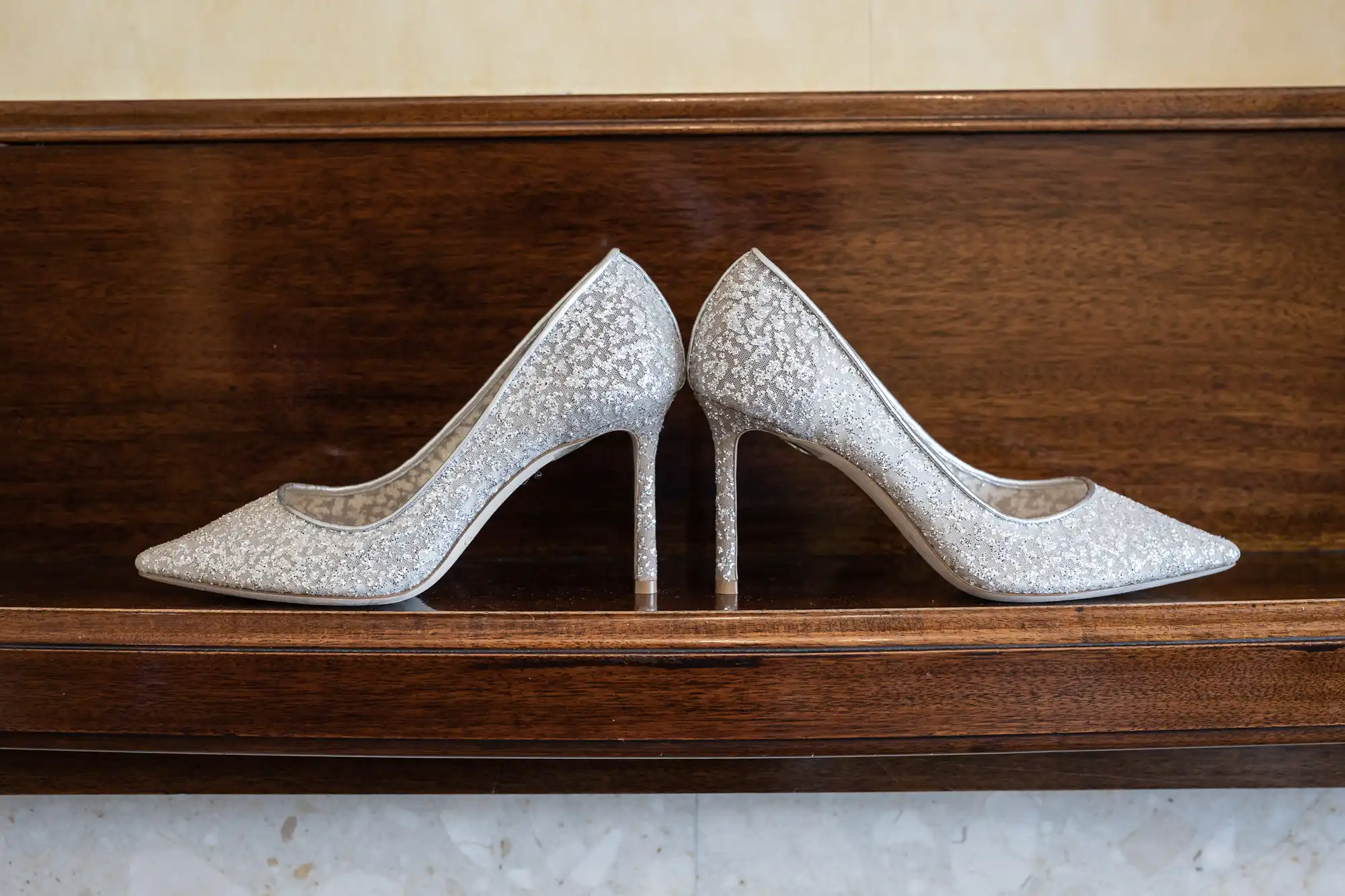 A pair of sparkly silver high-heeled shoes are placed together on a wooden surface.