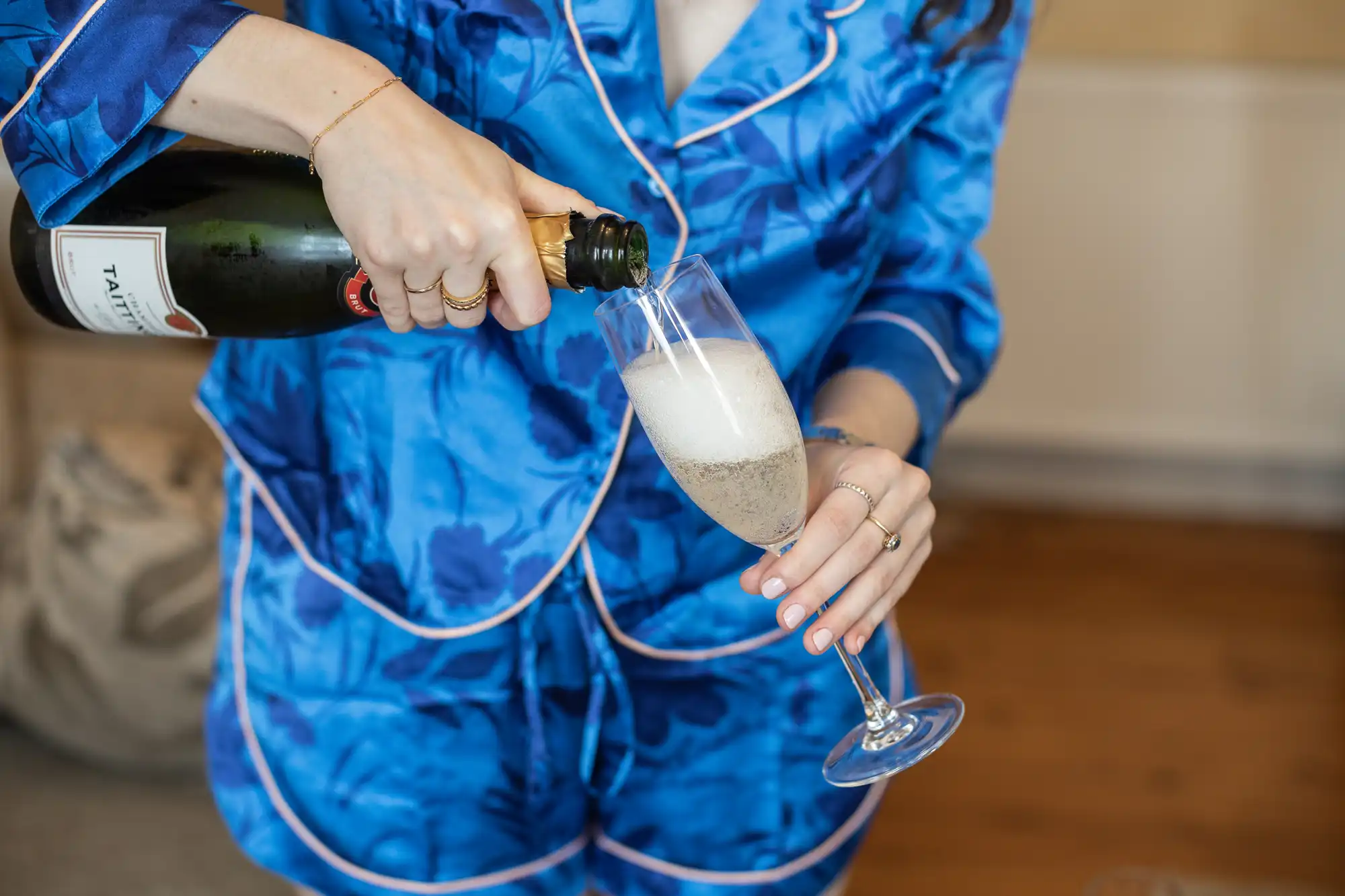 A person in blue pajamas pours champagne from a bottle into a flute glass.