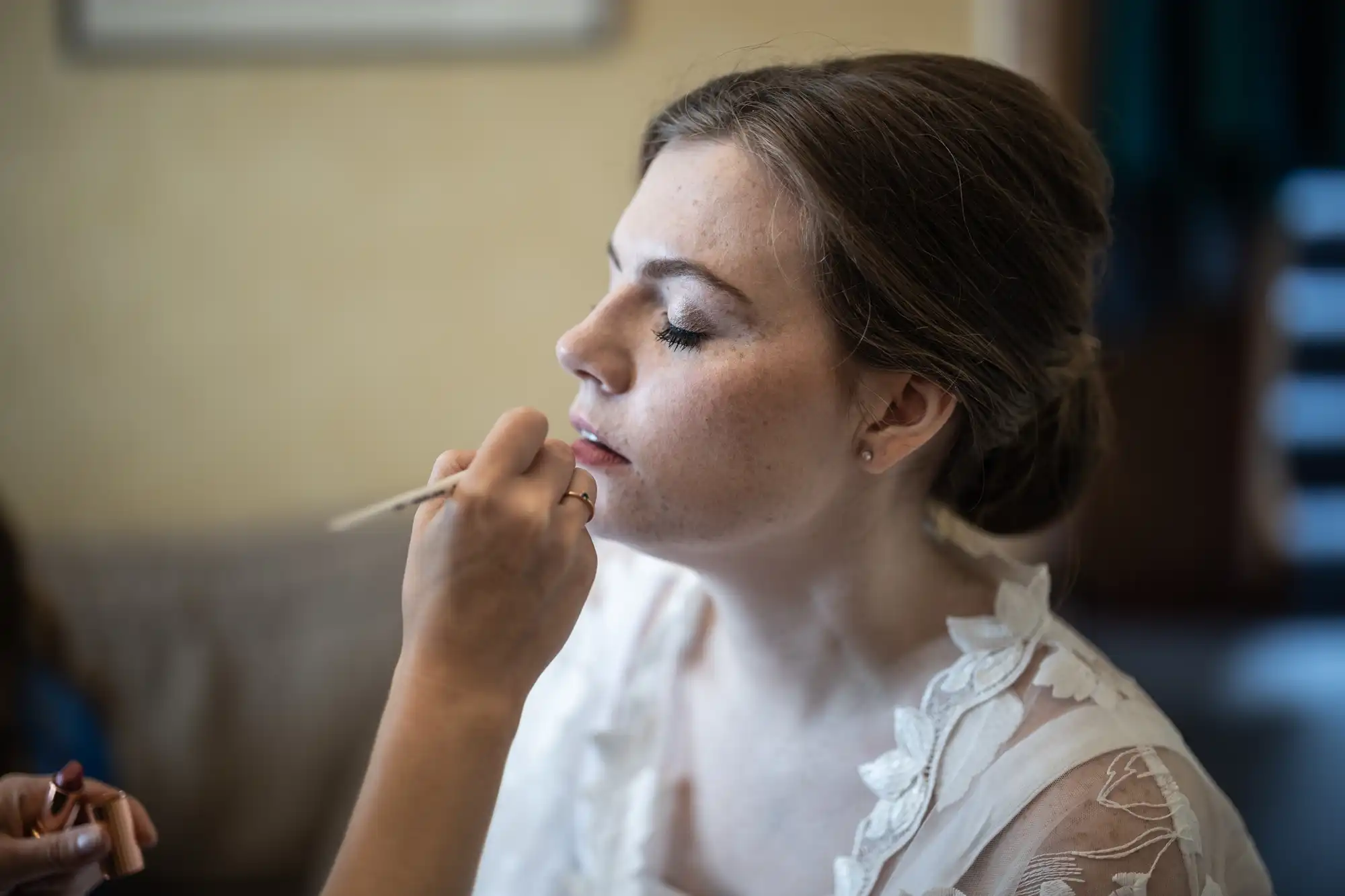 A person with eyes closed is getting makeup applied to their face by another person using a brush.