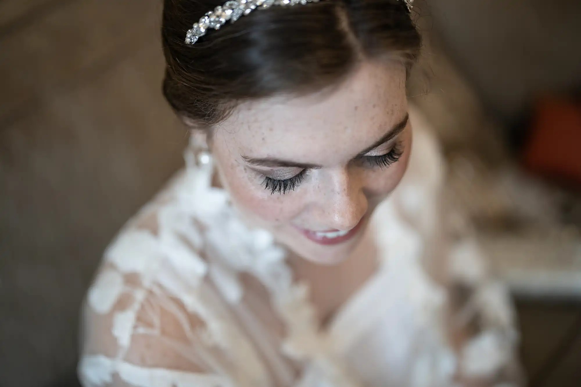 A bride with closed eyes and long lashes, wearing a delicate headband and lacy attire, smiling gently.