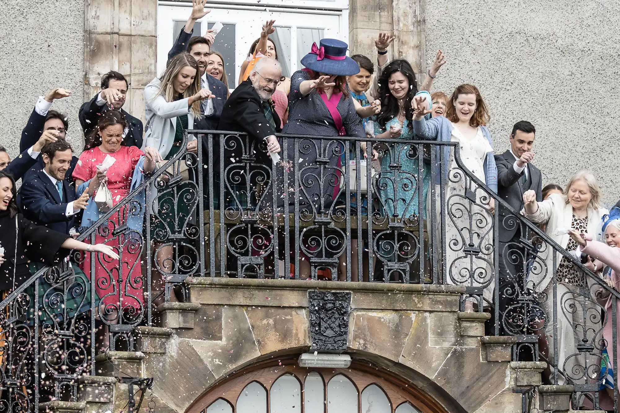 A group of people standing on a staircase, smiling and throwing confetti. The gathering appears festive, with various individuals dressed semi-formally.