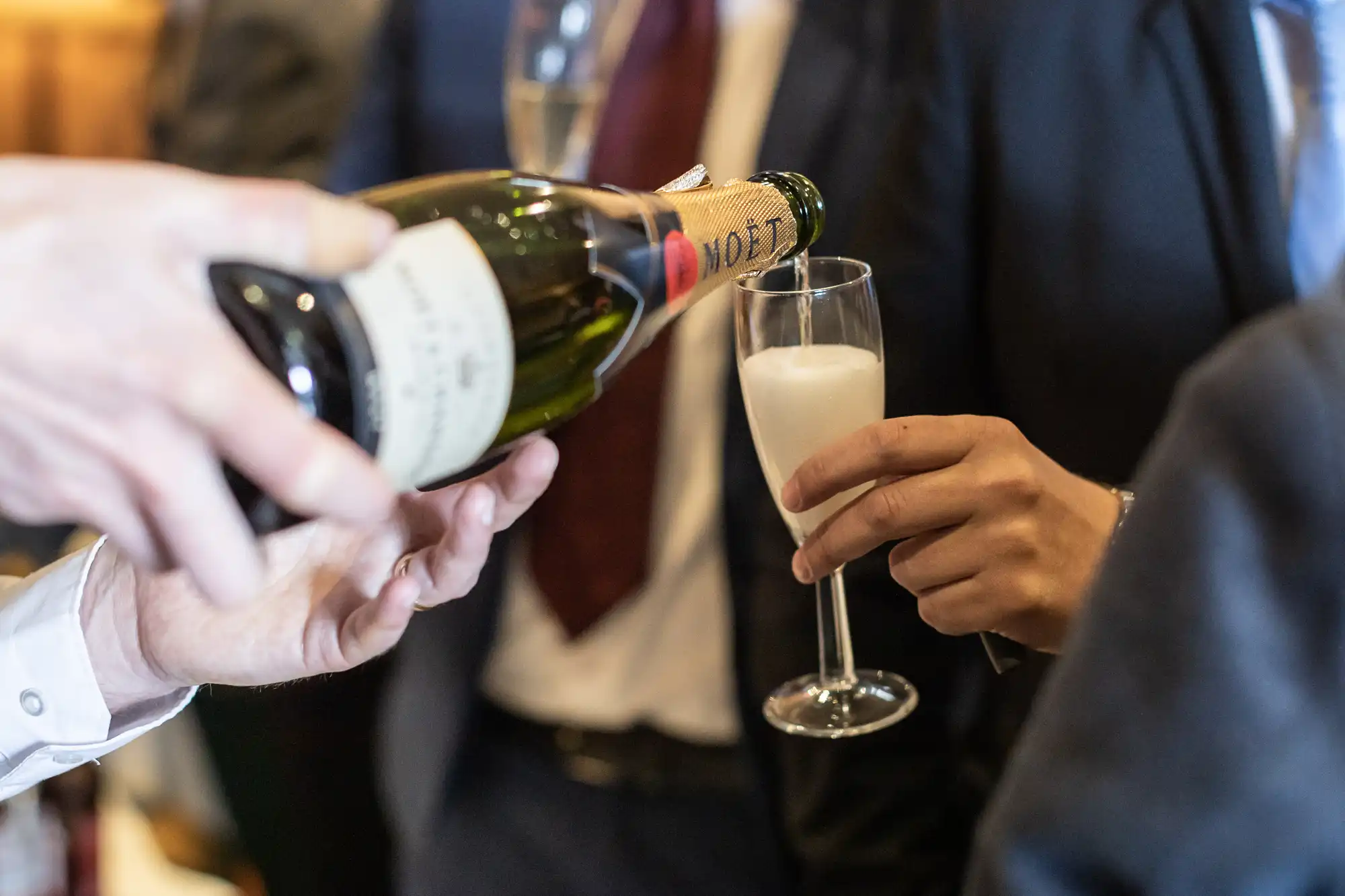 A person pours champagne from a Moët & Chandon bottle into a flute held by another individual in formal attire.