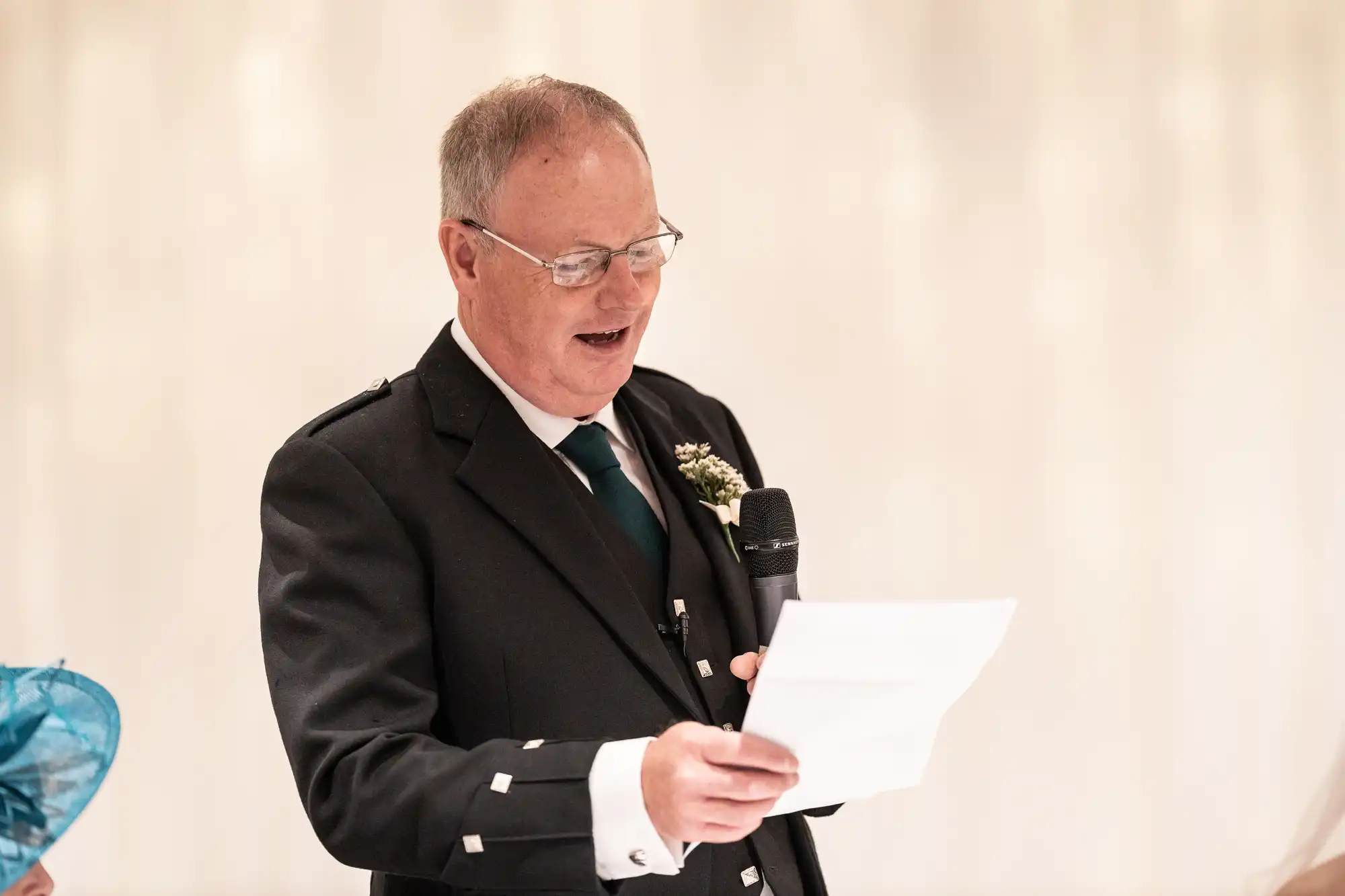 A man in a suit reads from a piece of paper while holding a microphone.