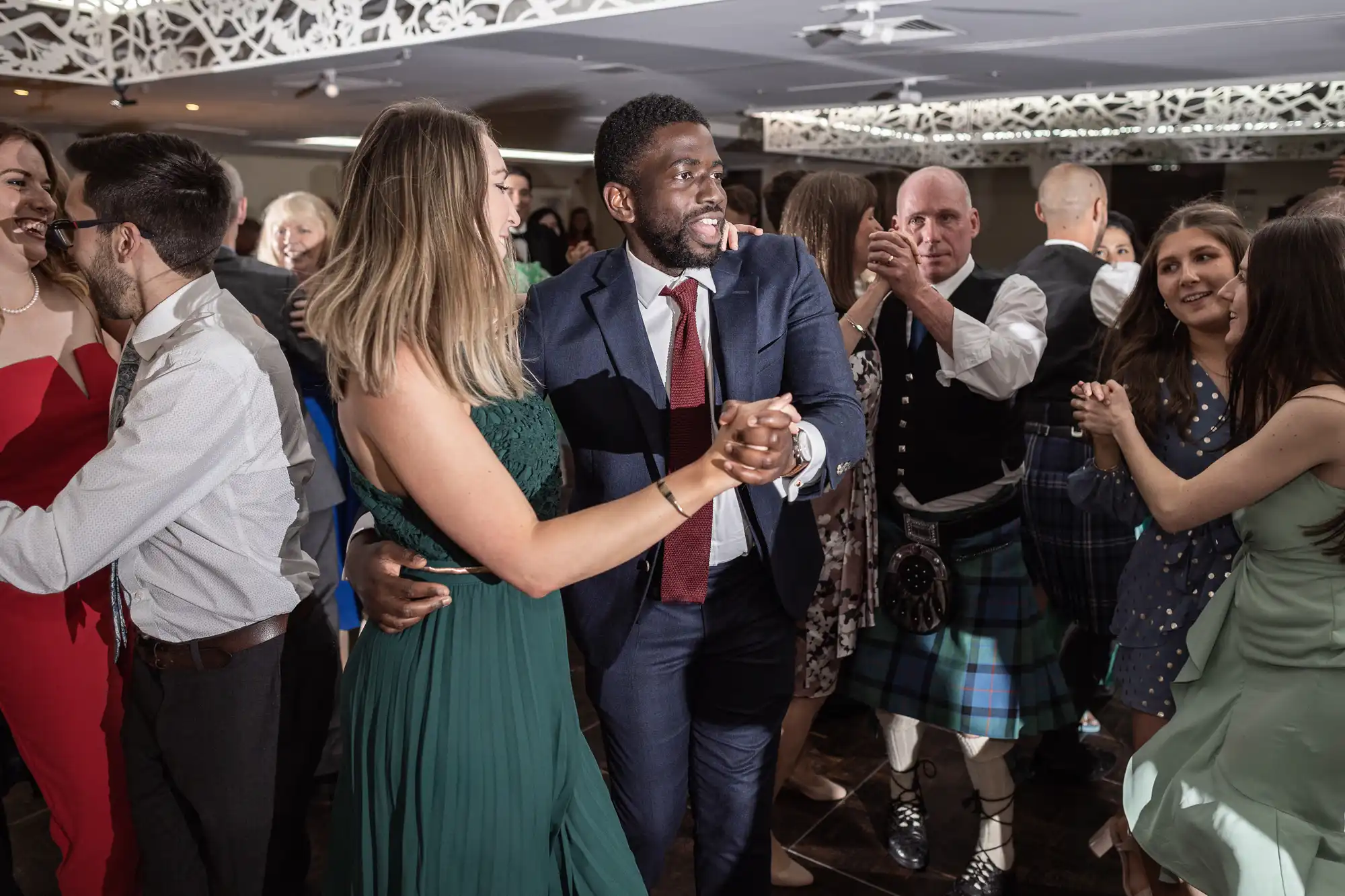 A group of people dancing in formal attire at a social event in a decorated indoor space.