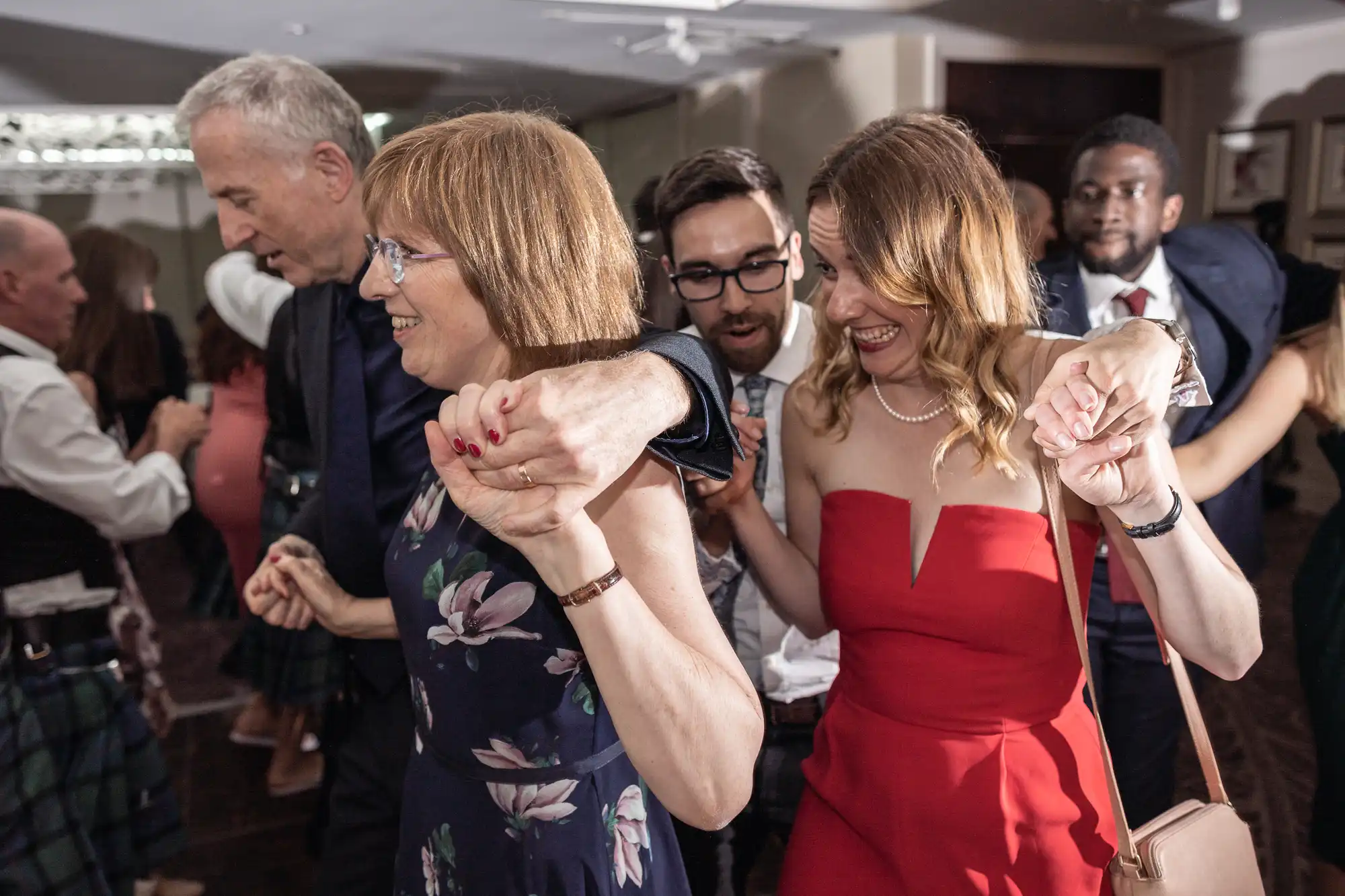 A group of people, dressed formally, are dancing together and holding hands in a lively setting.