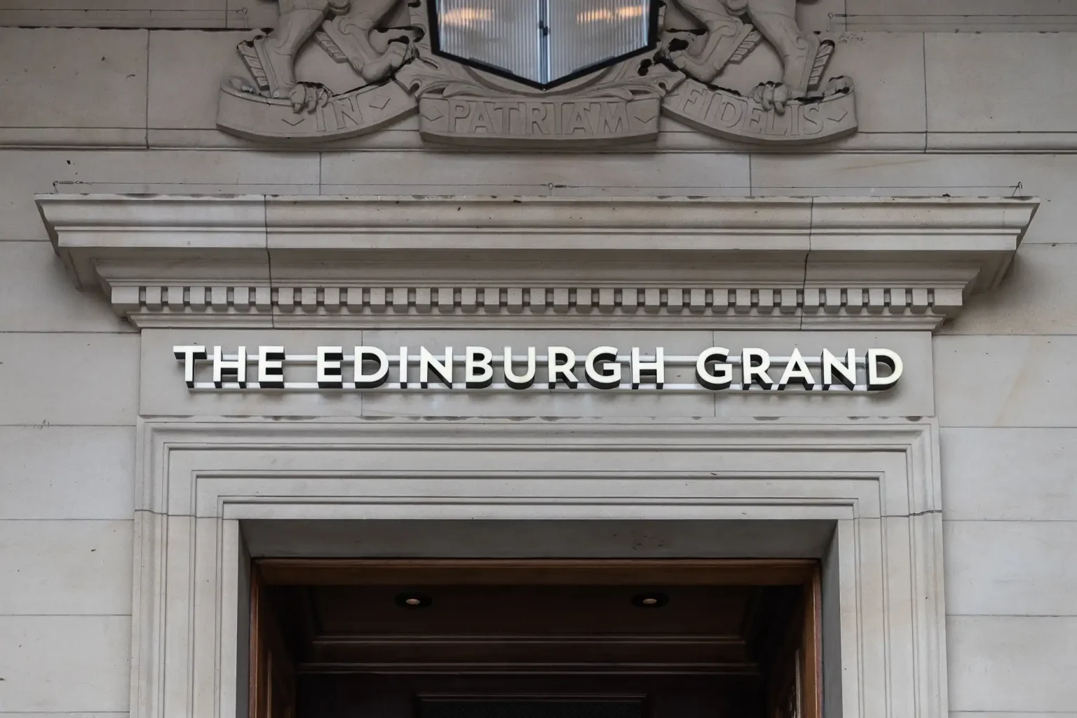 The Edinburgh Grand wedding photos: Entrance of the edinburgh grand with a prominent name sign displayed above the doorway, framed by a decorative stone pediment.