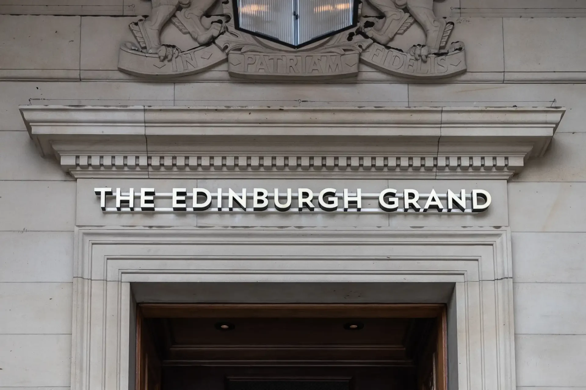Entrance of the edinburgh grand with a prominent name sign displayed above the doorway, framed by a decorative stone pediment.