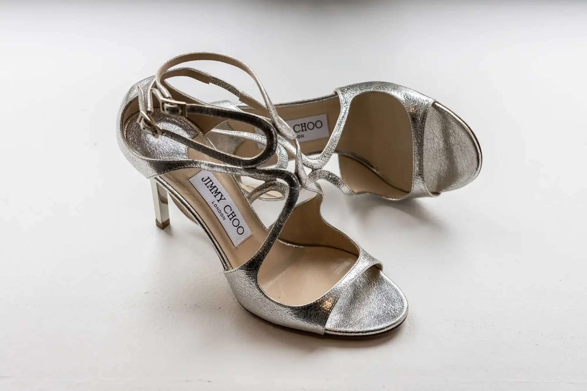 A pair of silver jimmy choo high heels on a white surface.