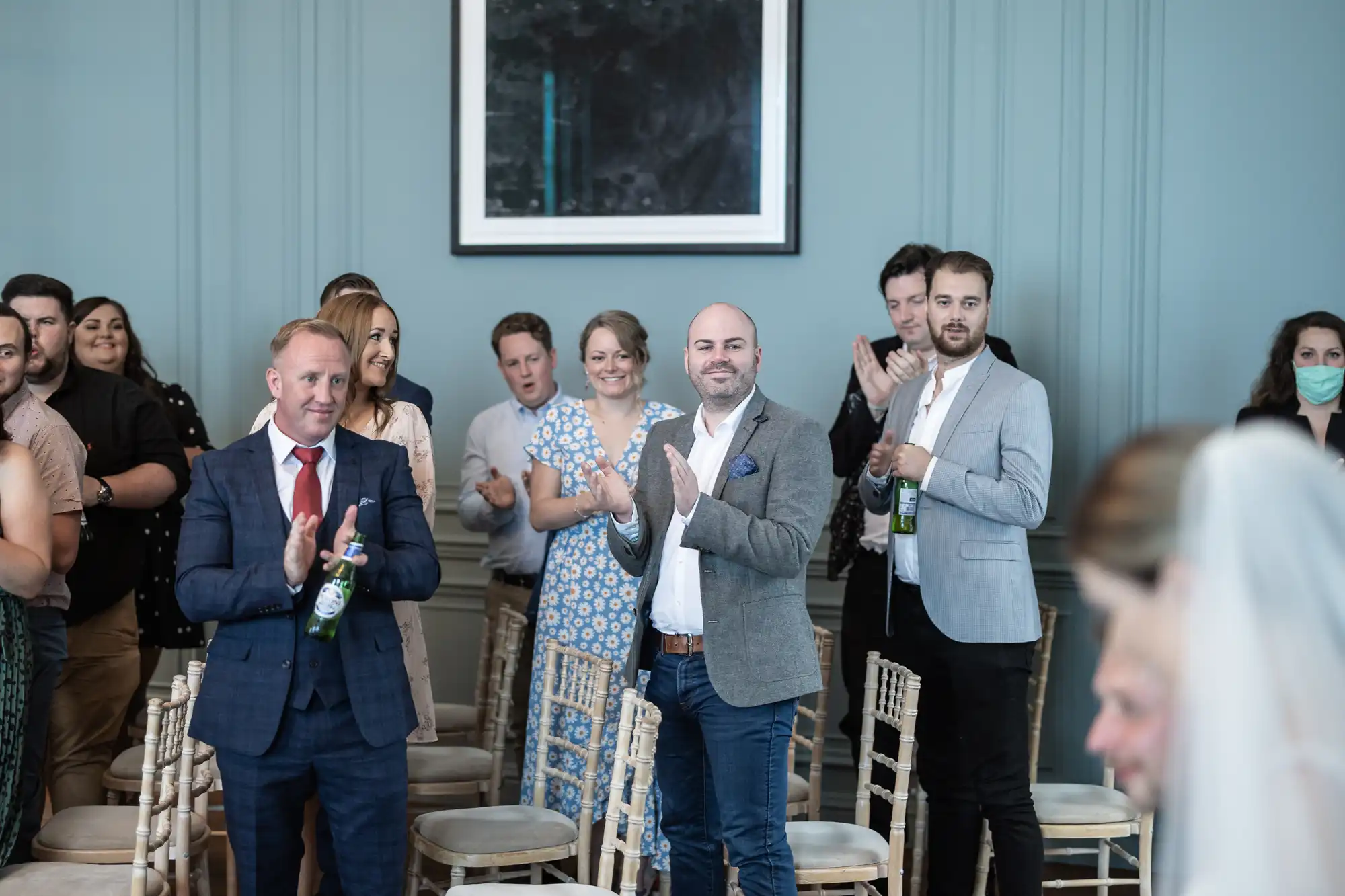 Guests clapping in a room with light blue walls and elegant chairs during a wedding ceremony.