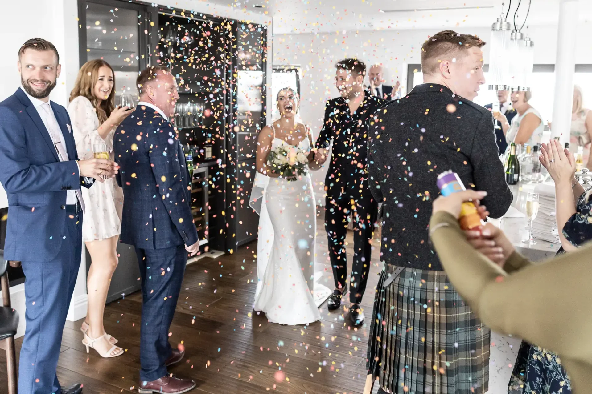 A joyful wedding scene with guests throwing confetti at the smiling bride and groom in a modern reception venue.