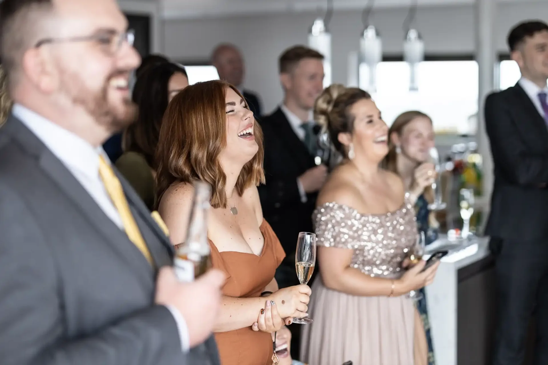 Group of formally dressed people laughing and holding drinks at a social gathering indoors.