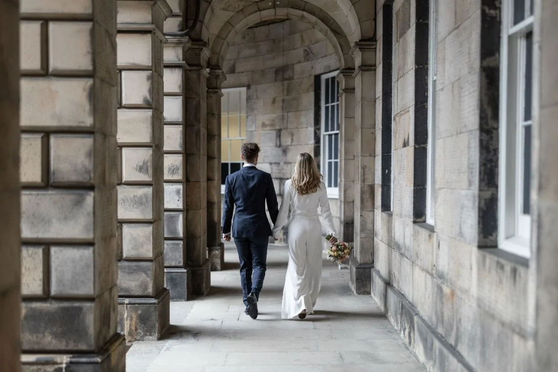 bride and groom holding hands under the arches at the Signet Library