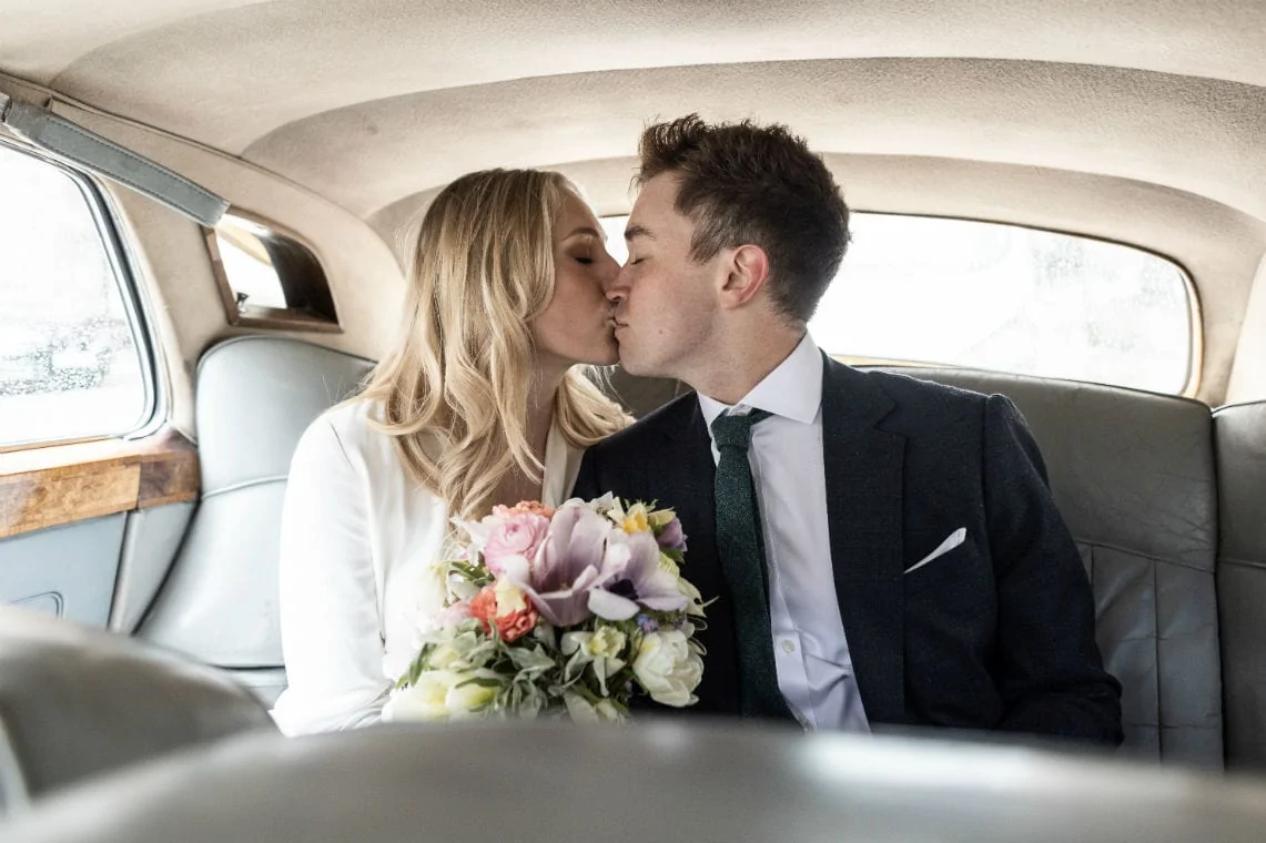 newlyweds kissing in the back of a classic Bentley