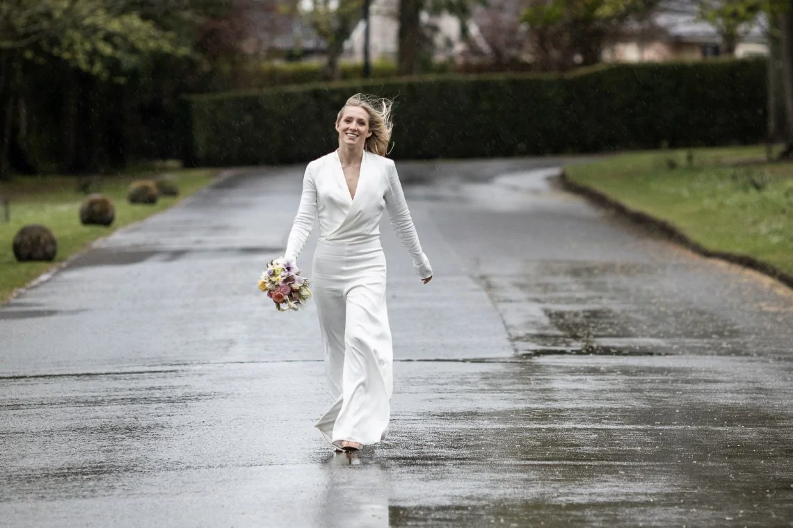 bride in a white jumpsuit walking along the avenue