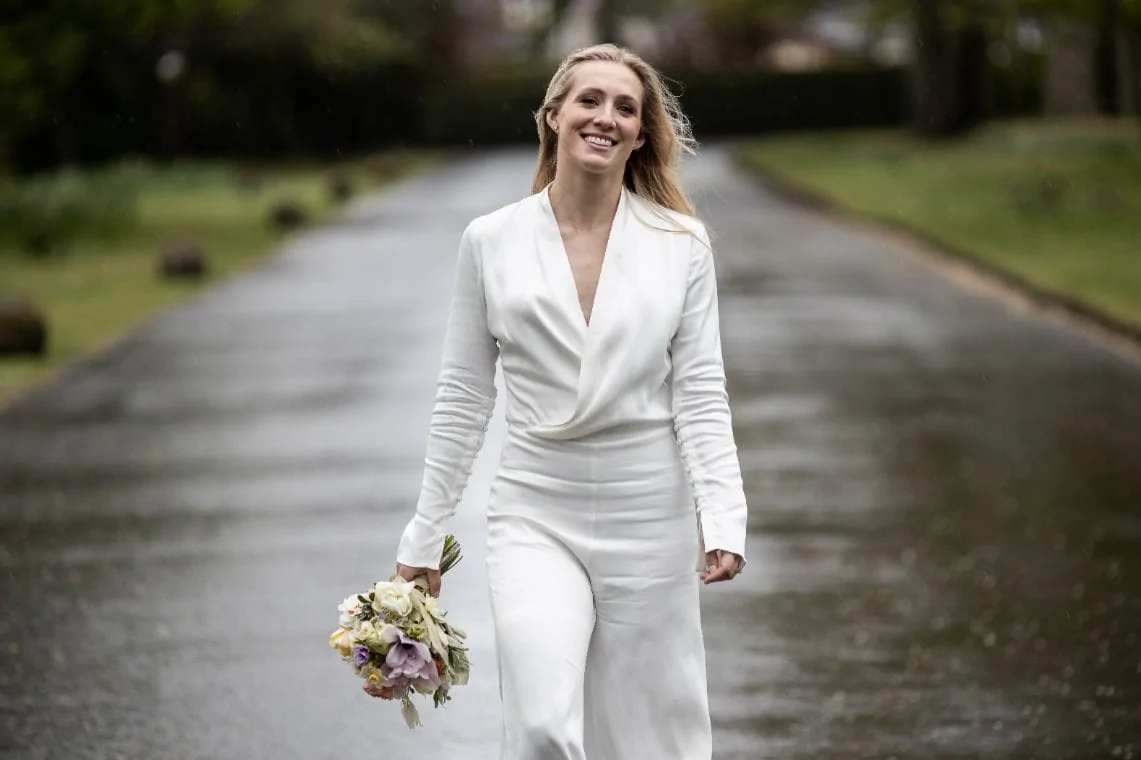 bride in a white jumpsuit walking along the avenue