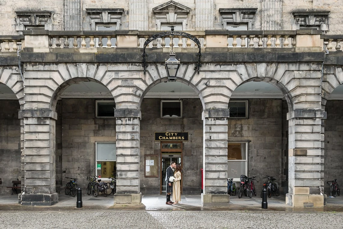newlyweds embrace under the arches of the Quadrant at City Chambers in the rain
