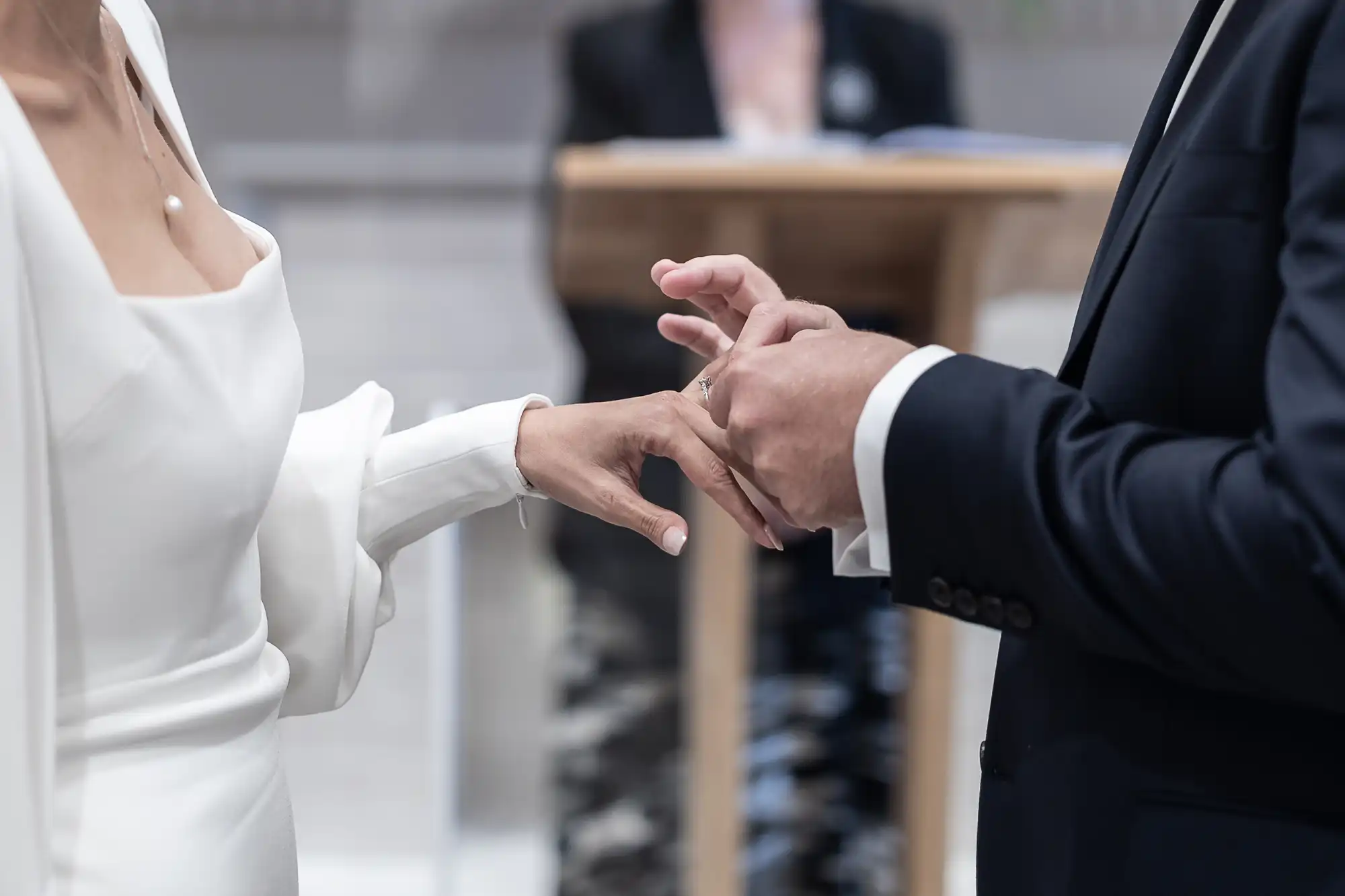 A bride and groom exchanging rings during their wedding ceremony, with an officiant visible in the background.