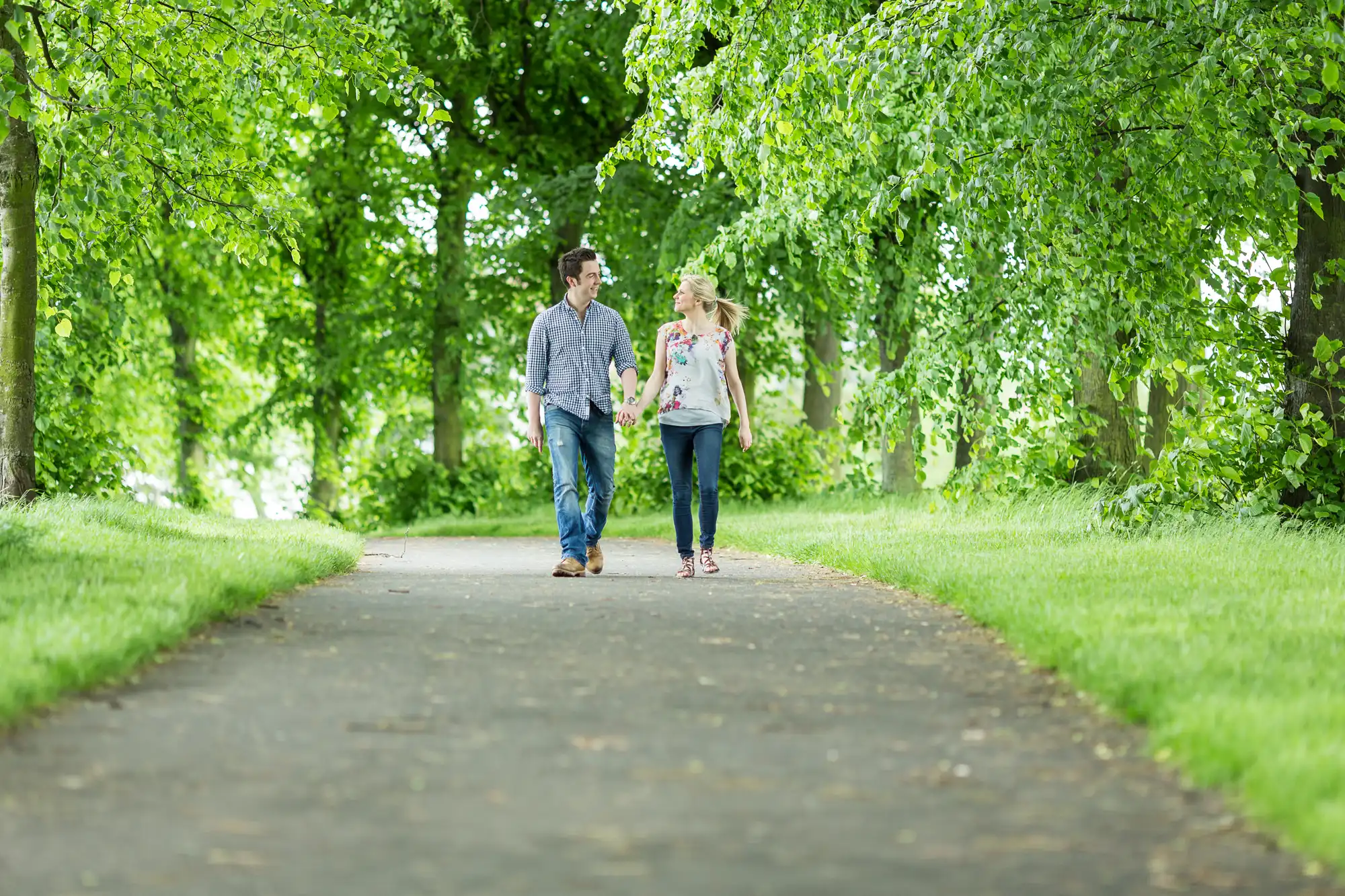 A man and a woman walking and talking on a tree-lined pathway in a park.