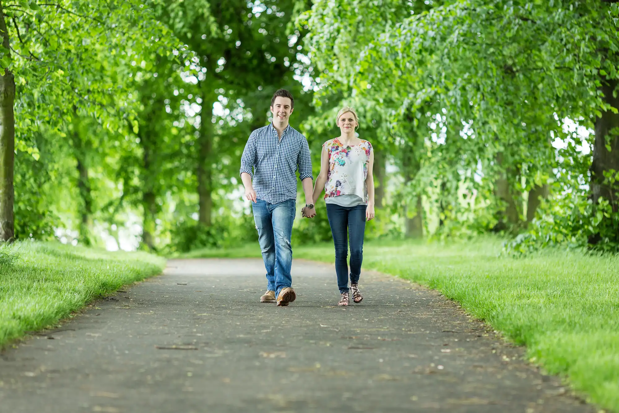A man and a woman walking happily together down a tree-lined path in a lush green park.