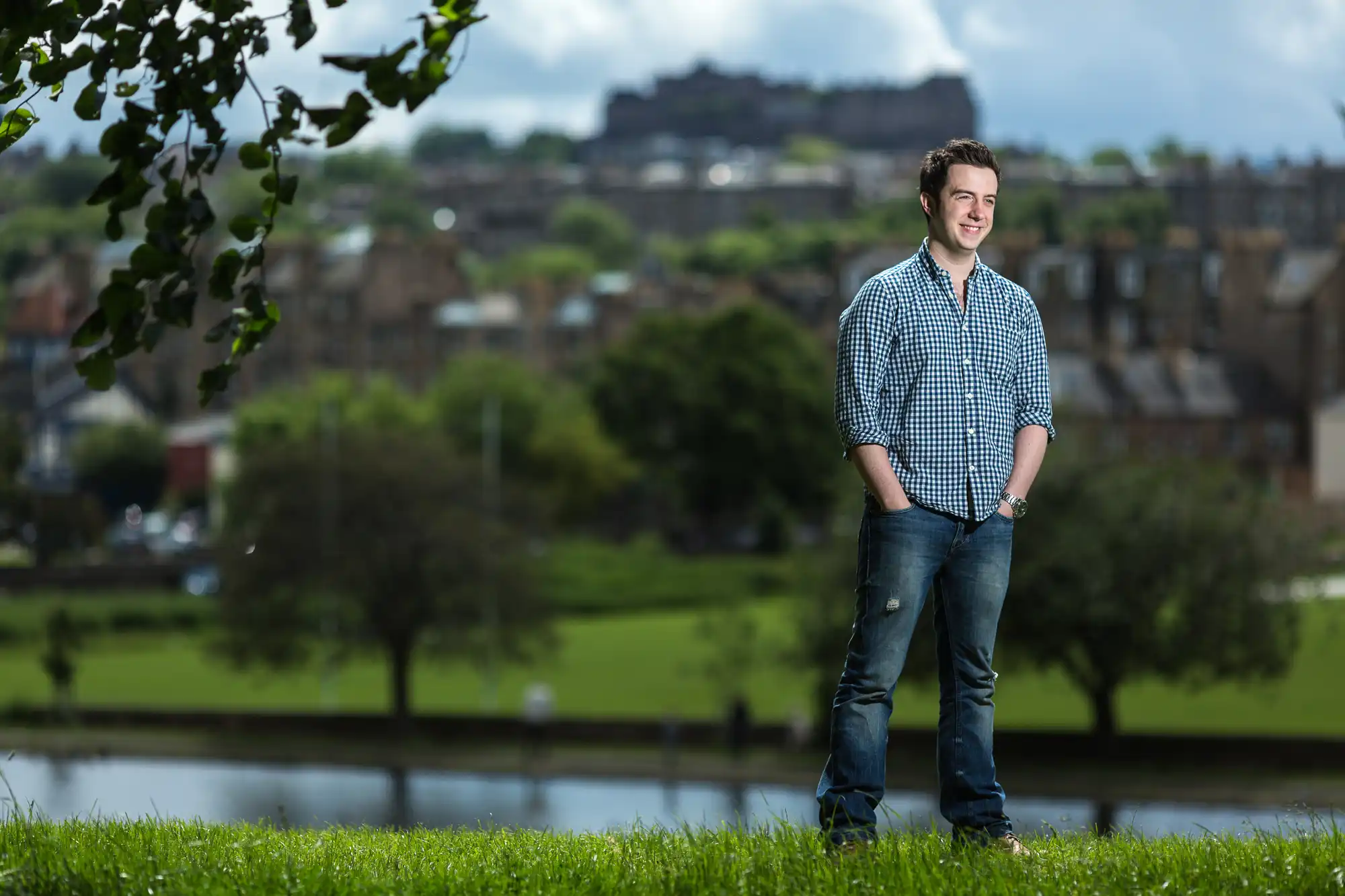 Young man standing in a park with the cityscape and edinburgh castle in the background on a cloudy day.